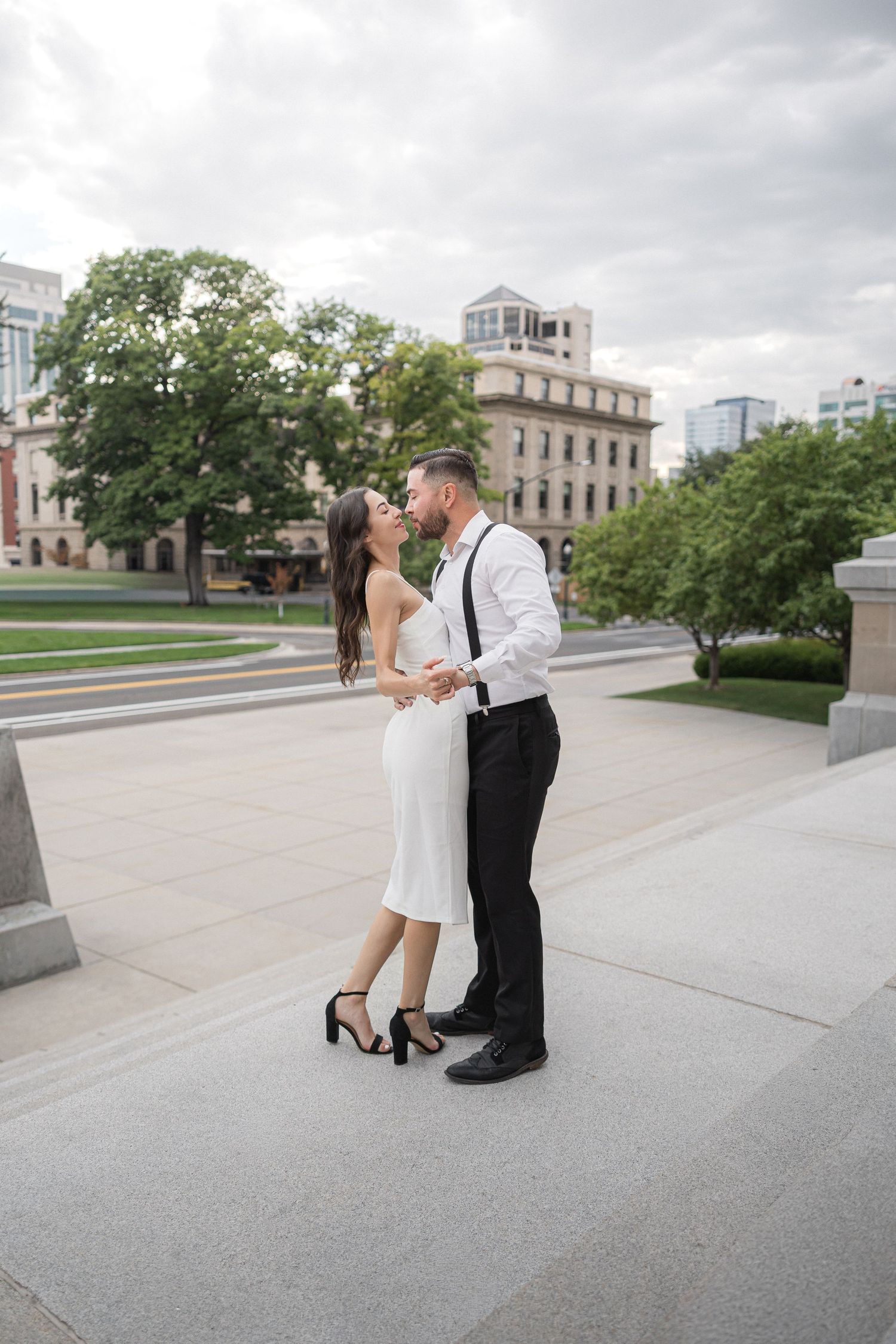 Couple in formal attire dances on concrete plaza with urban backdrop.