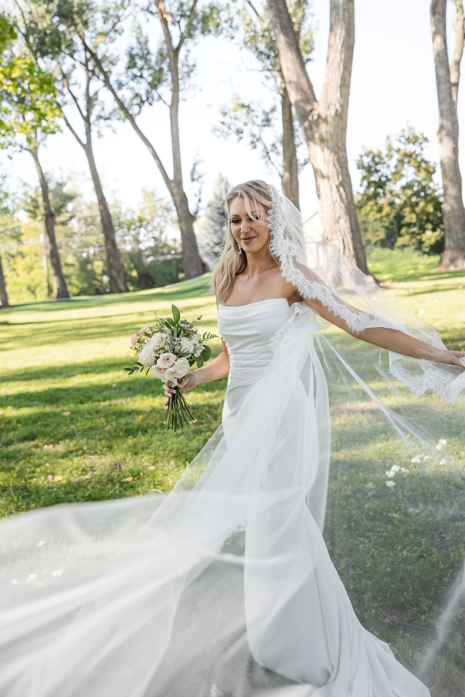 A bride twirls in her flowing white dress with veil catching the sunlight.