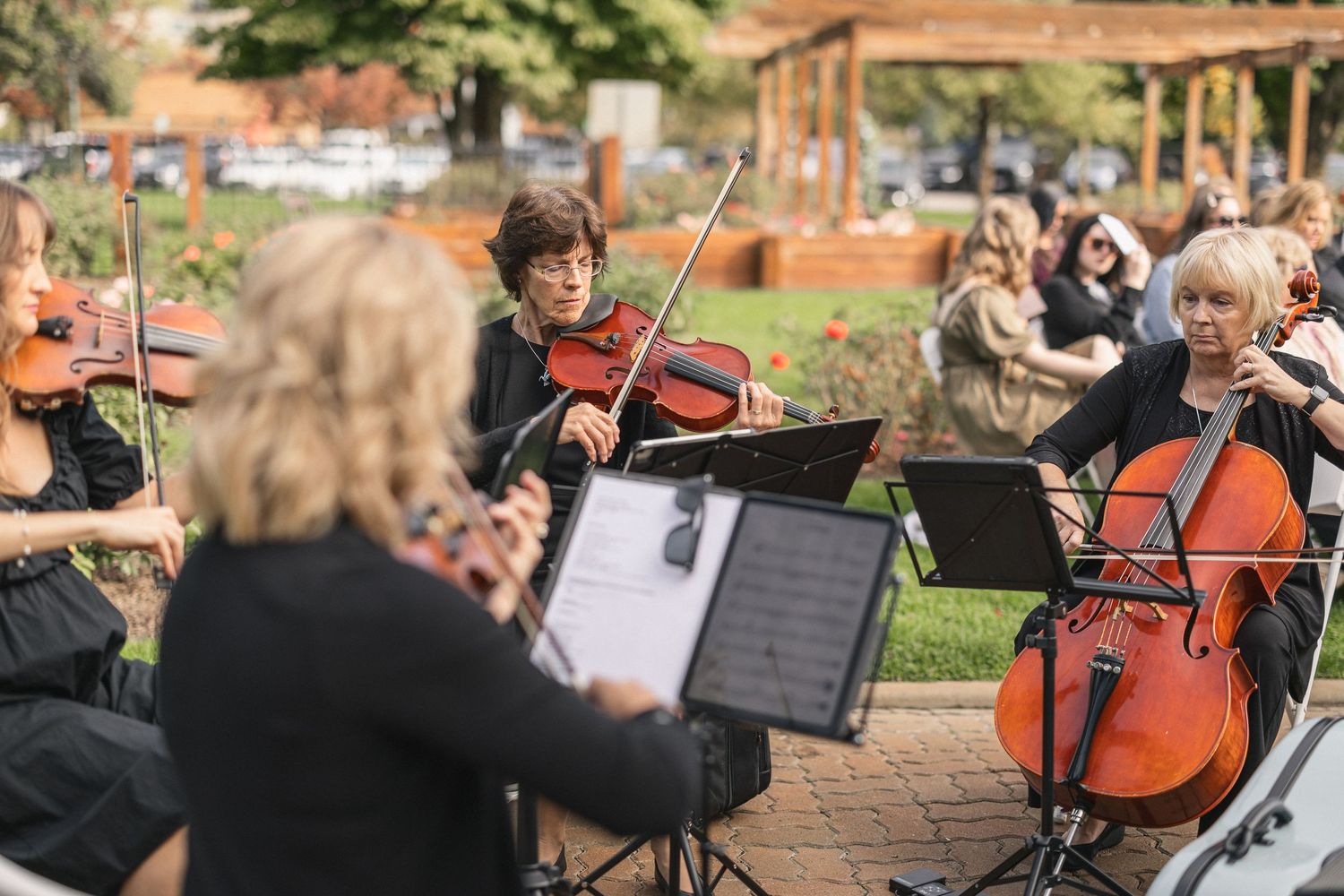 String quartet performs outdoors in a garden setting with music stands and sheet music.