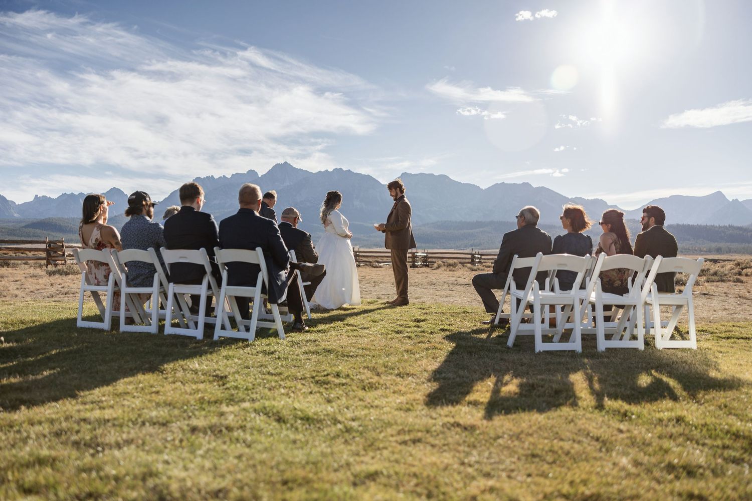 Wedding guests seated in white chairs for an outdoor ceremony with mountain vistas.