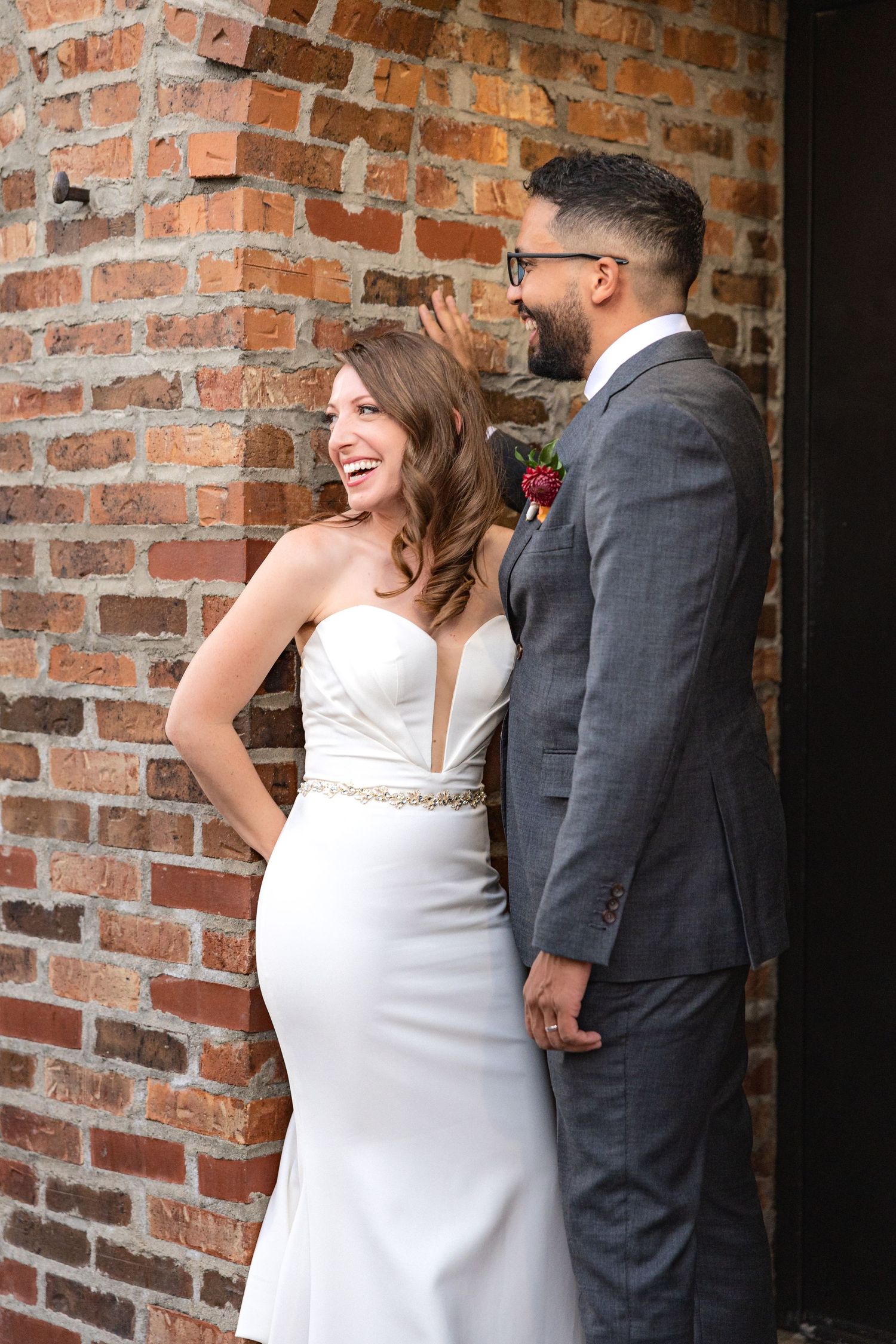 Candid moment of couple laughing together against brick wall background.