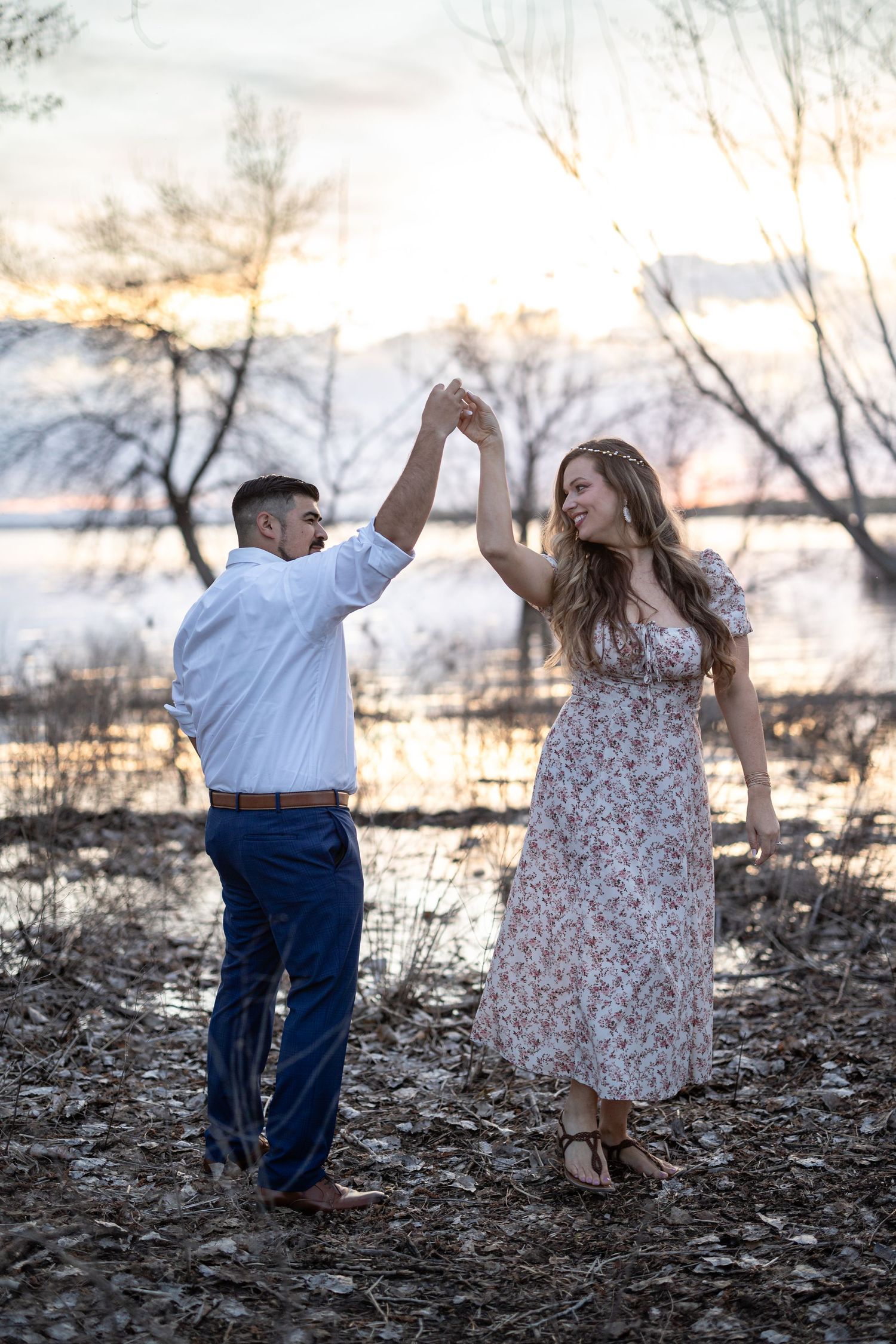 Couple dances playfully together on a rocky shoreline during golden hour.