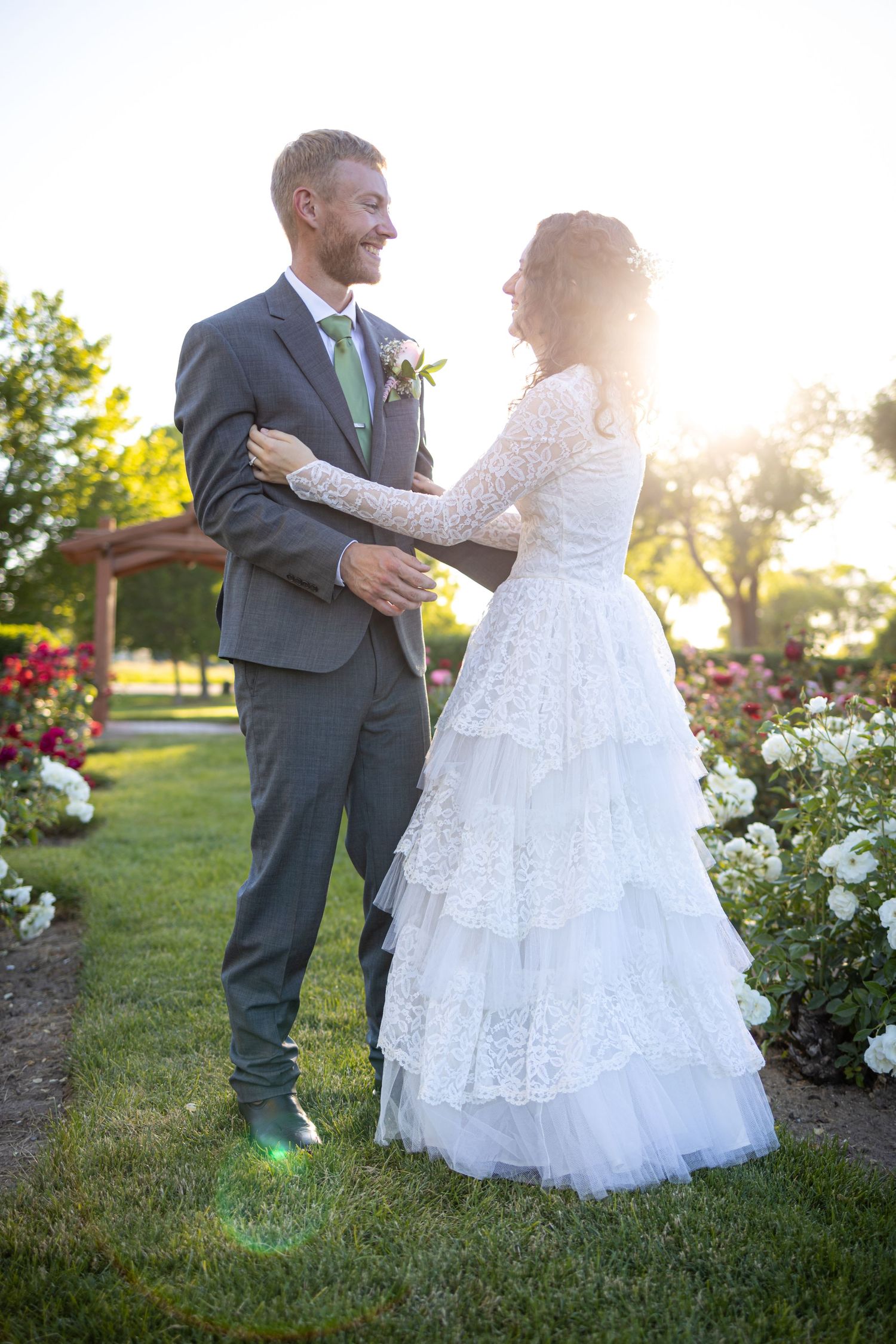 A romantic wedding couple embraces outdoors in a garden at sunset with beautiful floral landscaping.