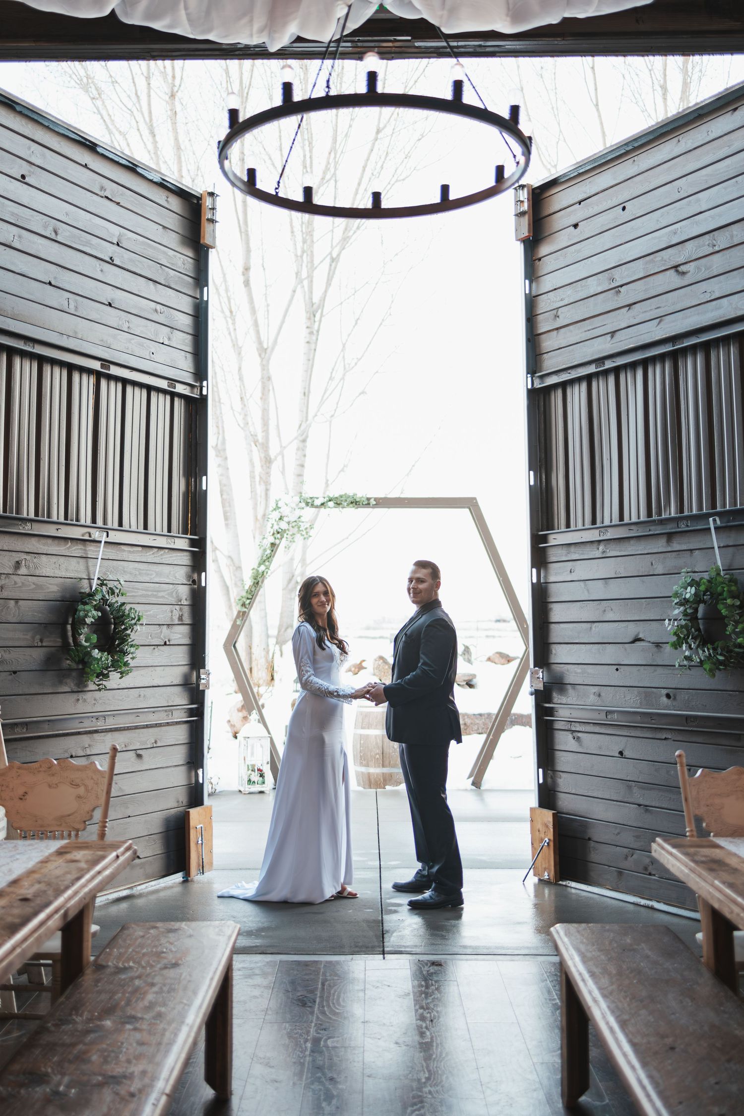 Couple exchanging vows in modern industrial chapel with hexagonal arch and rustic wooden benches.