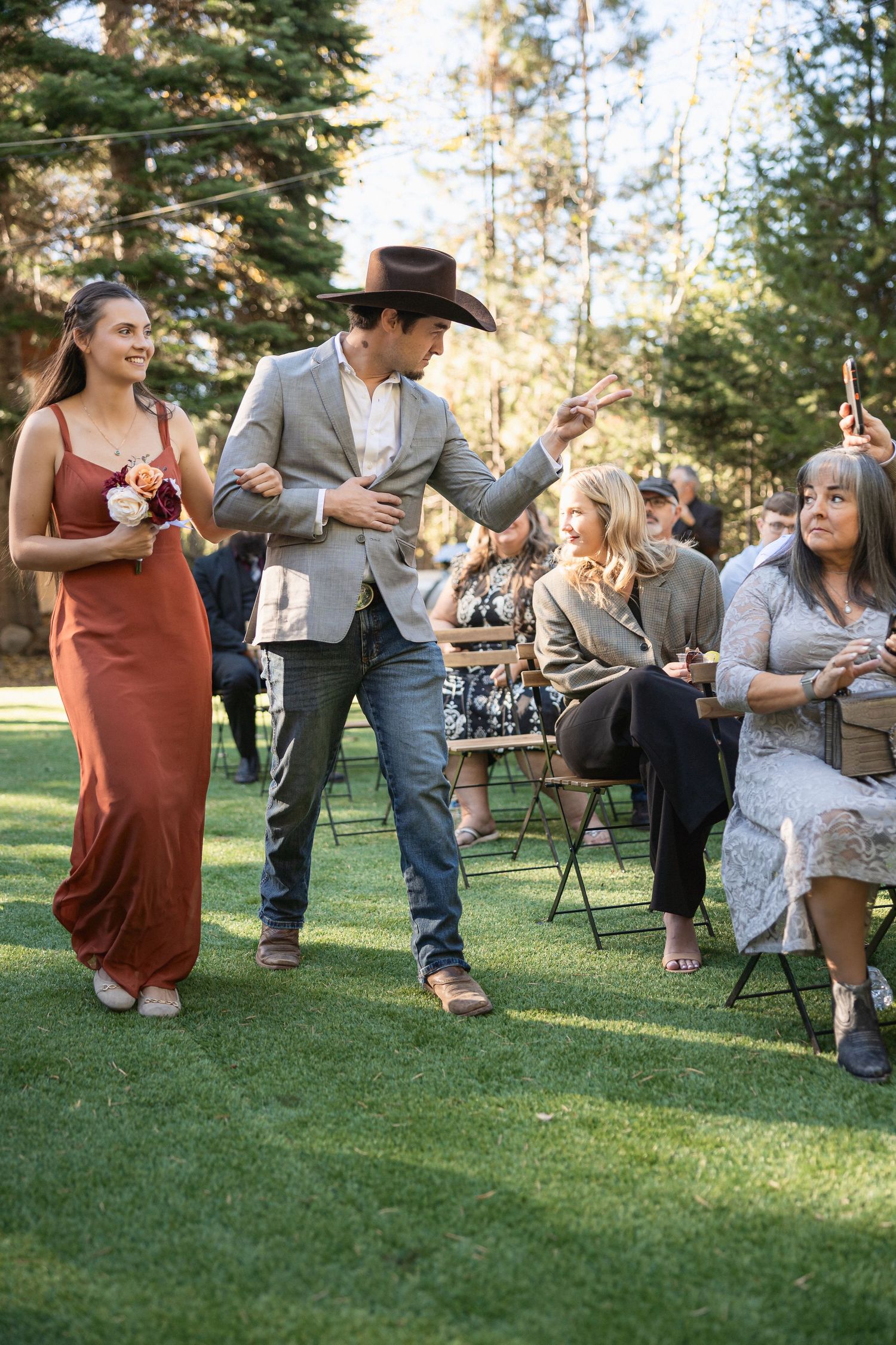Wedding party members walking during outdoor ceremony with guests seated on lawn.