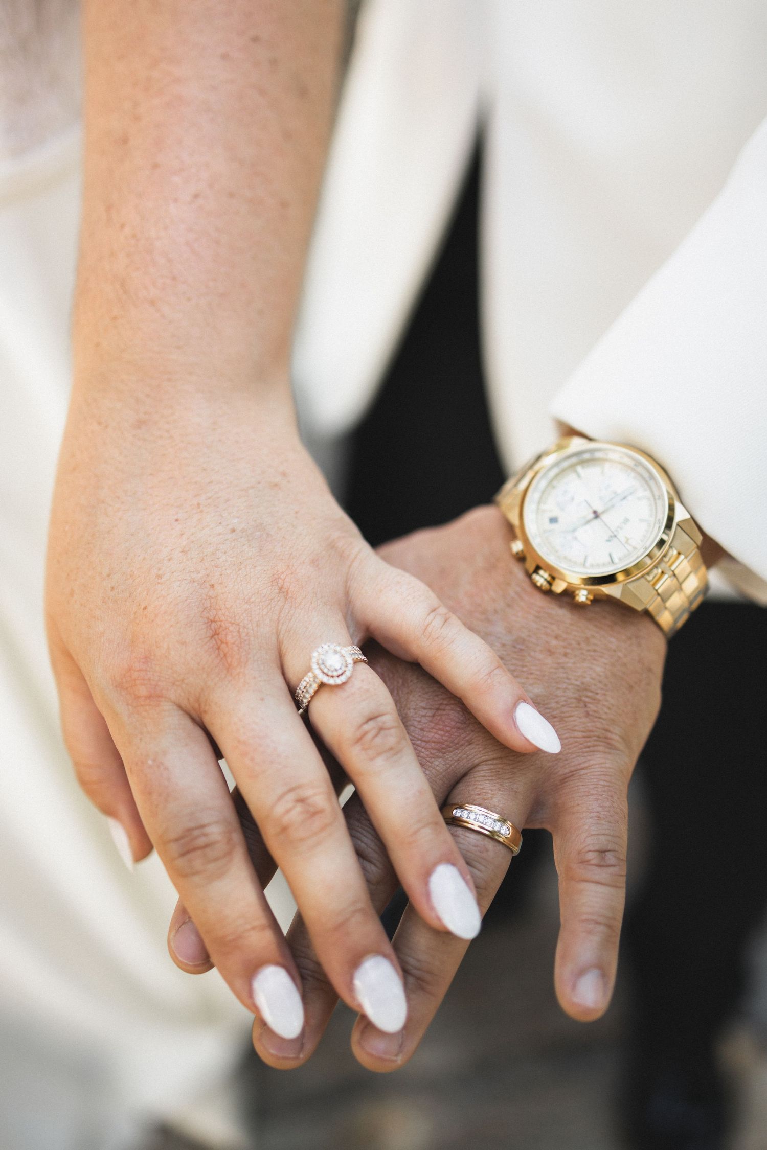 Close-up of wedding rings and white nail polish with a gold watch detail.