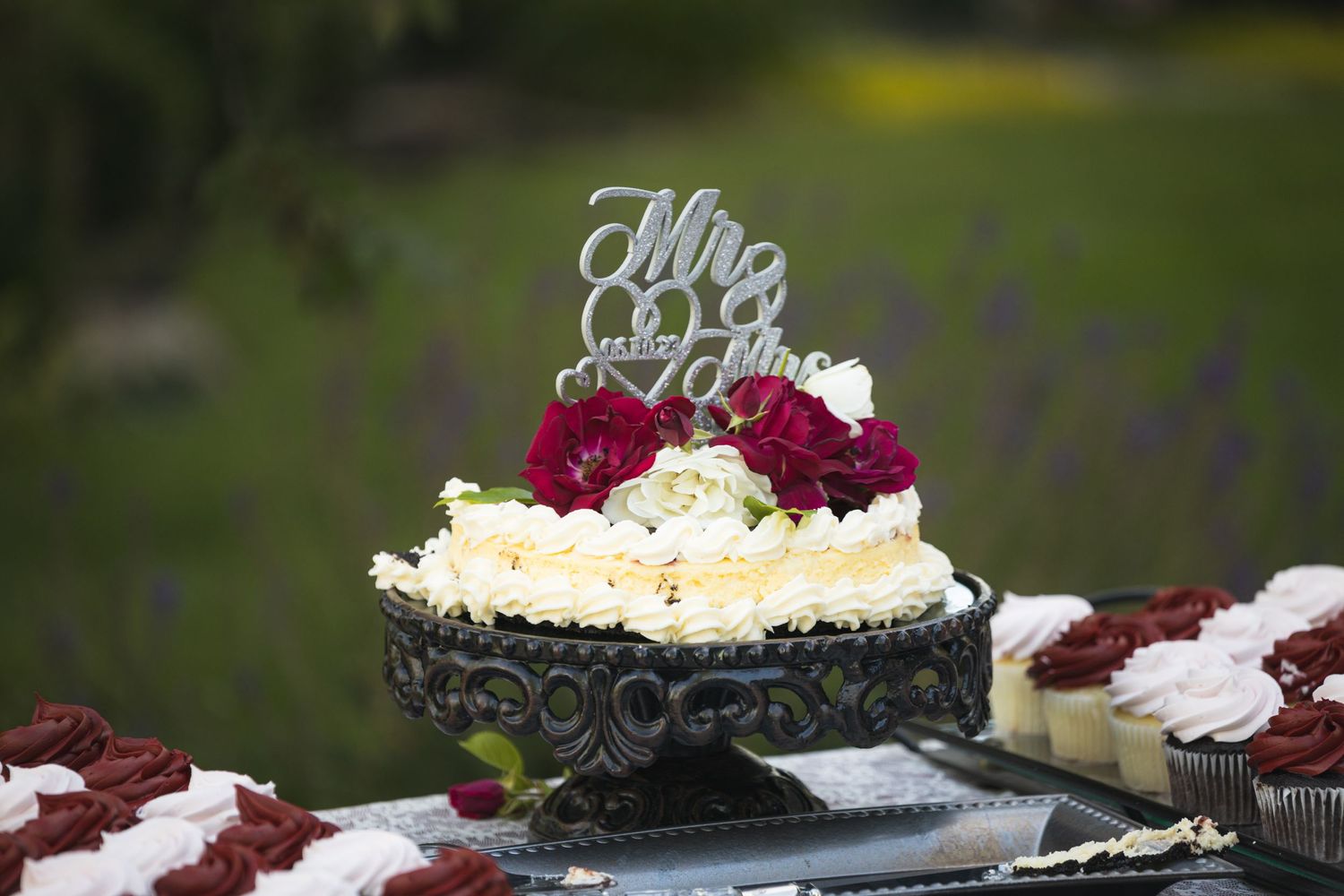 An elegant wedding cake topped with 'Mr & Mrs' sits on a black pedestal with burgundy floral accents.