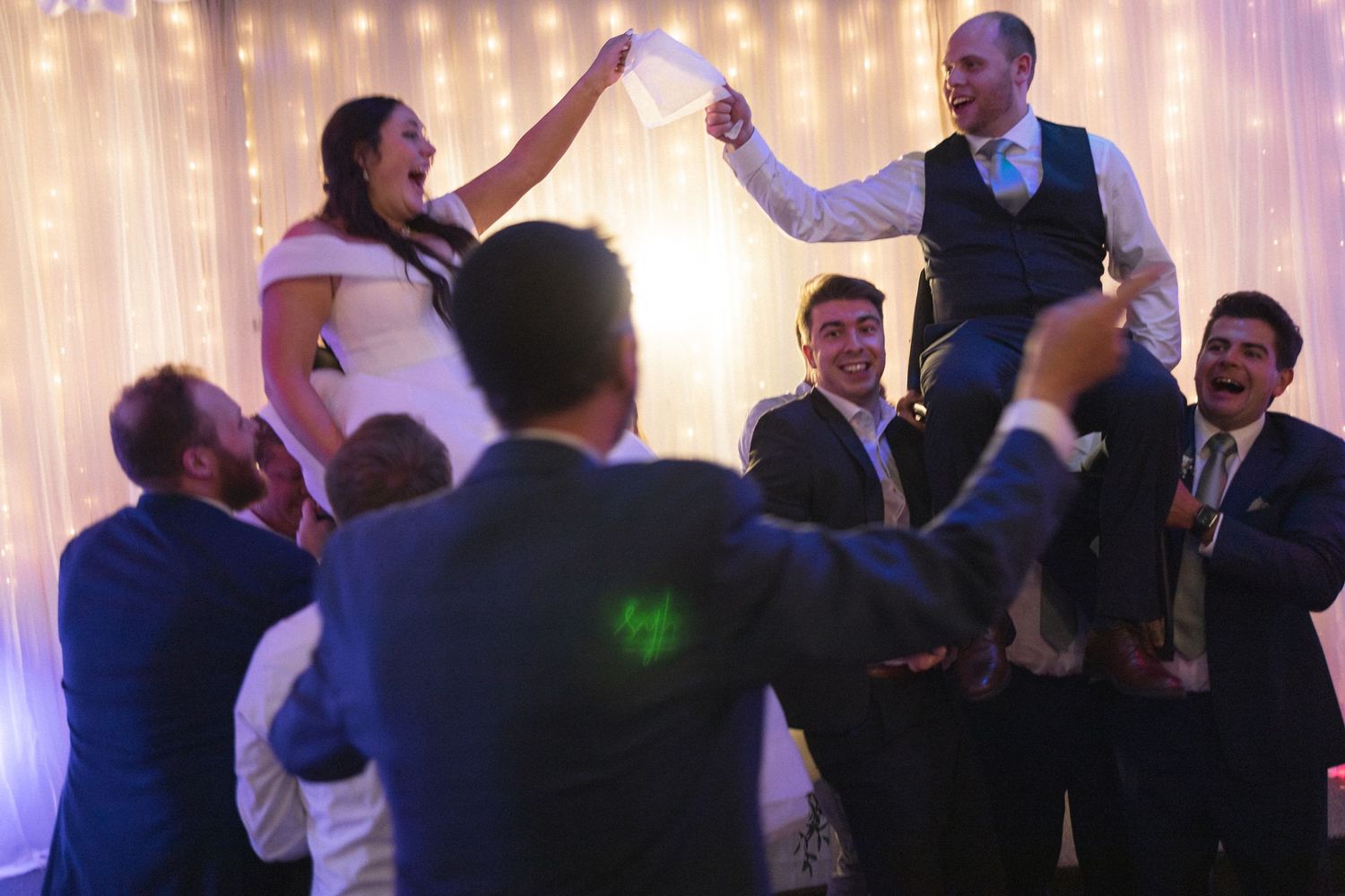 Groomsmen lift the newlyweds on their shoulders during a lively wedding reception dance.