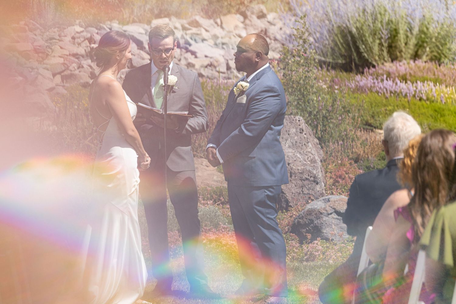 Outdoor wedding celebration with rainbow lens flare effect in garden setting.