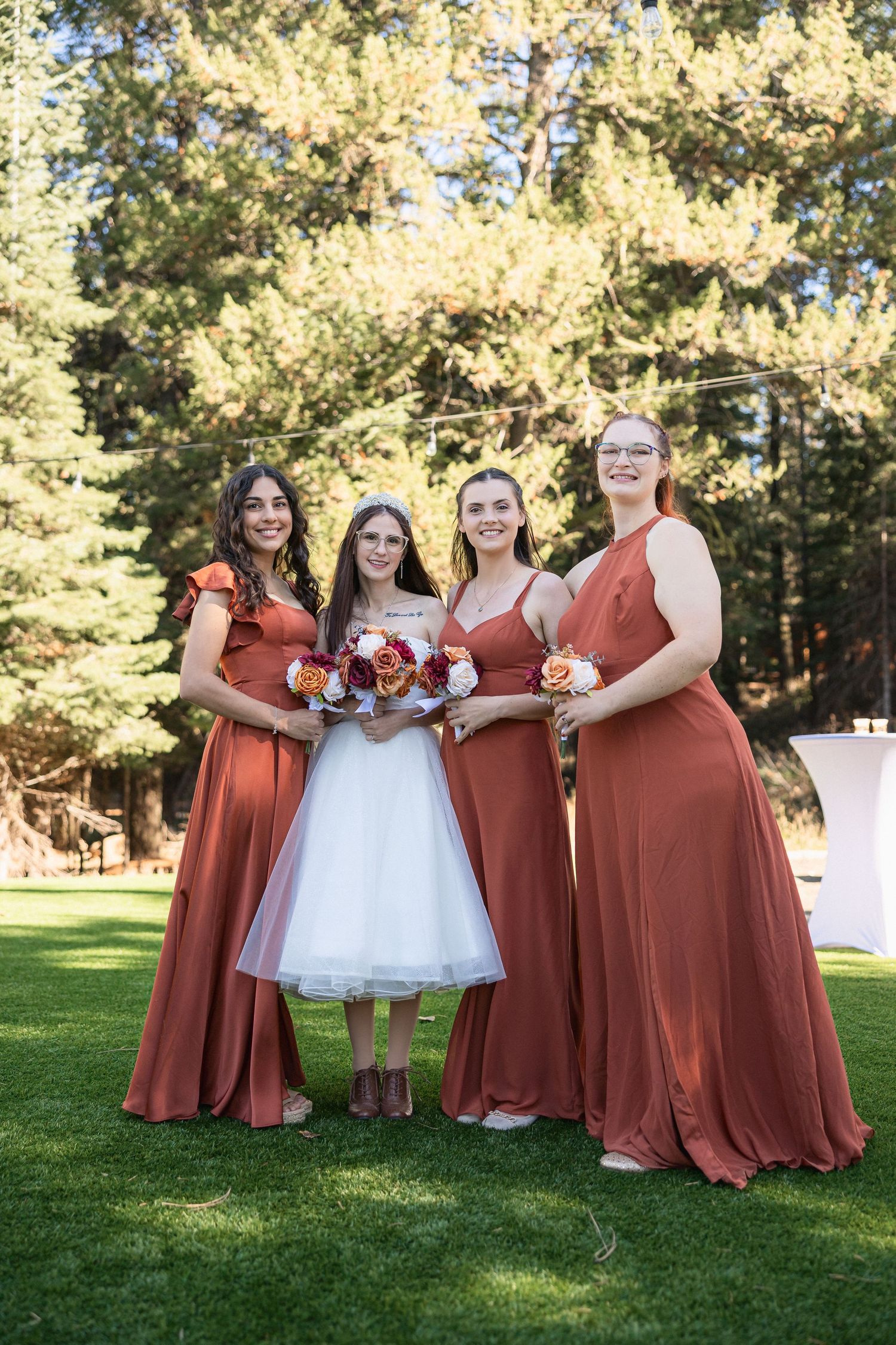 Bridesmaids in rust-colored dresses posing together on grass lawn.