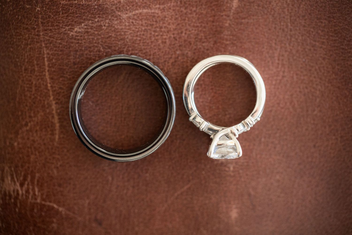 Wedding rings on brown leather surface showing white gold engagement ring and dark band.