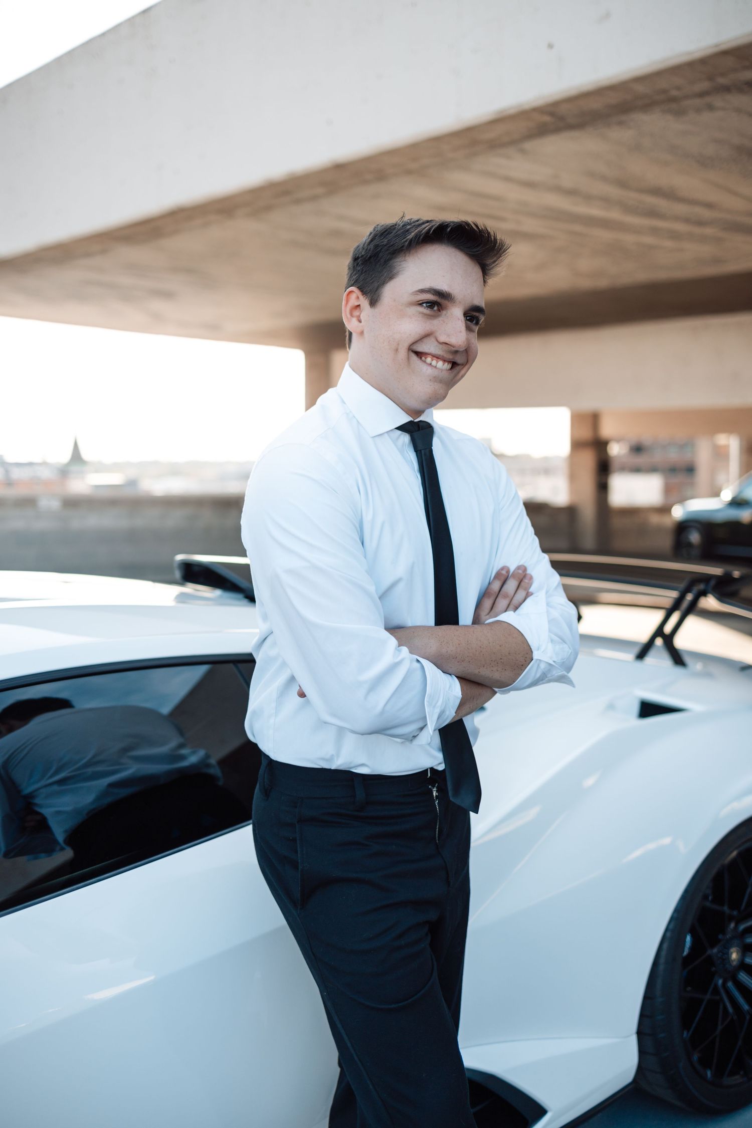 Person in white shirt and tie leans against white sports car in modern parking structure.