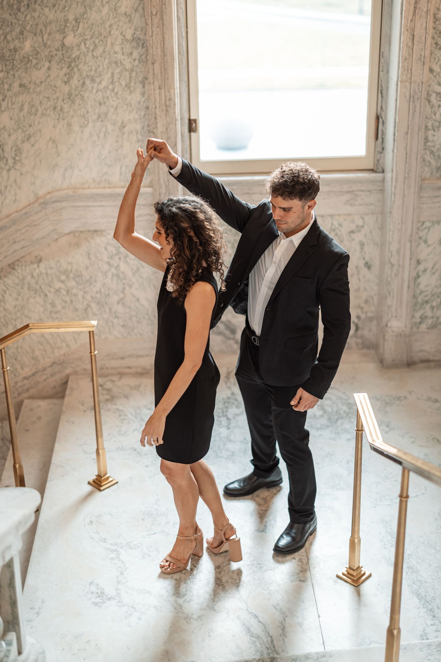 A couple shares a dance in formal attire within a marble-walled elegant interior.