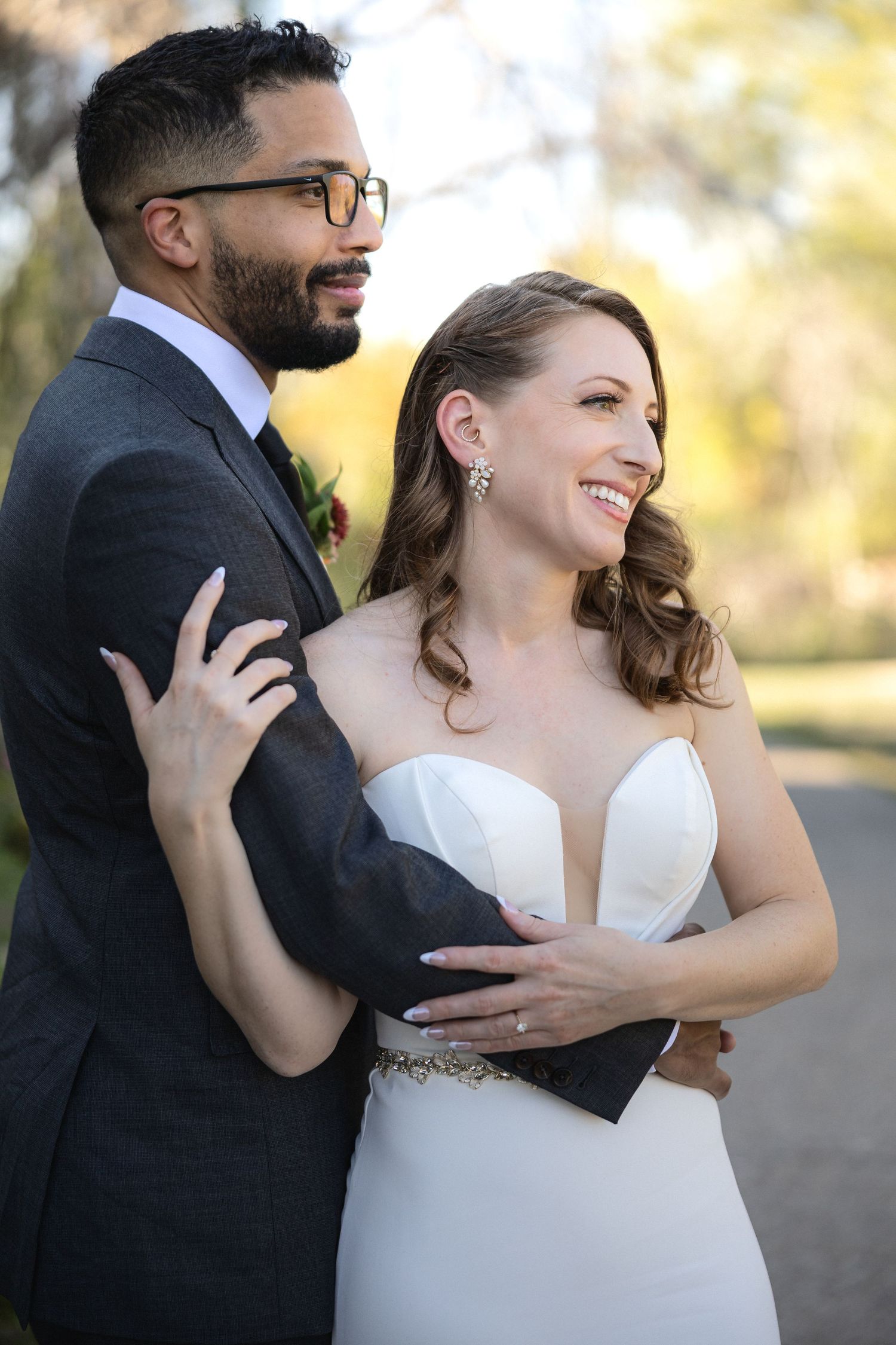 Joyful wedding couple sharing a candid moment in elegant attire against autumn backdrop.