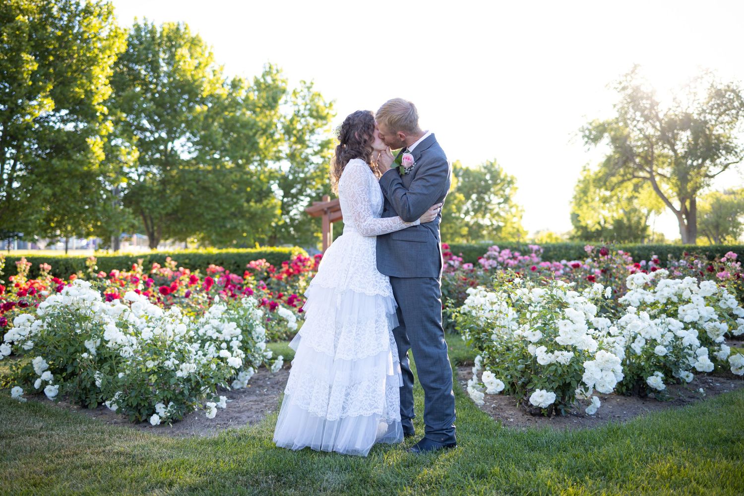 Intimate moment between newlyweds in rose garden with sunset lighting.