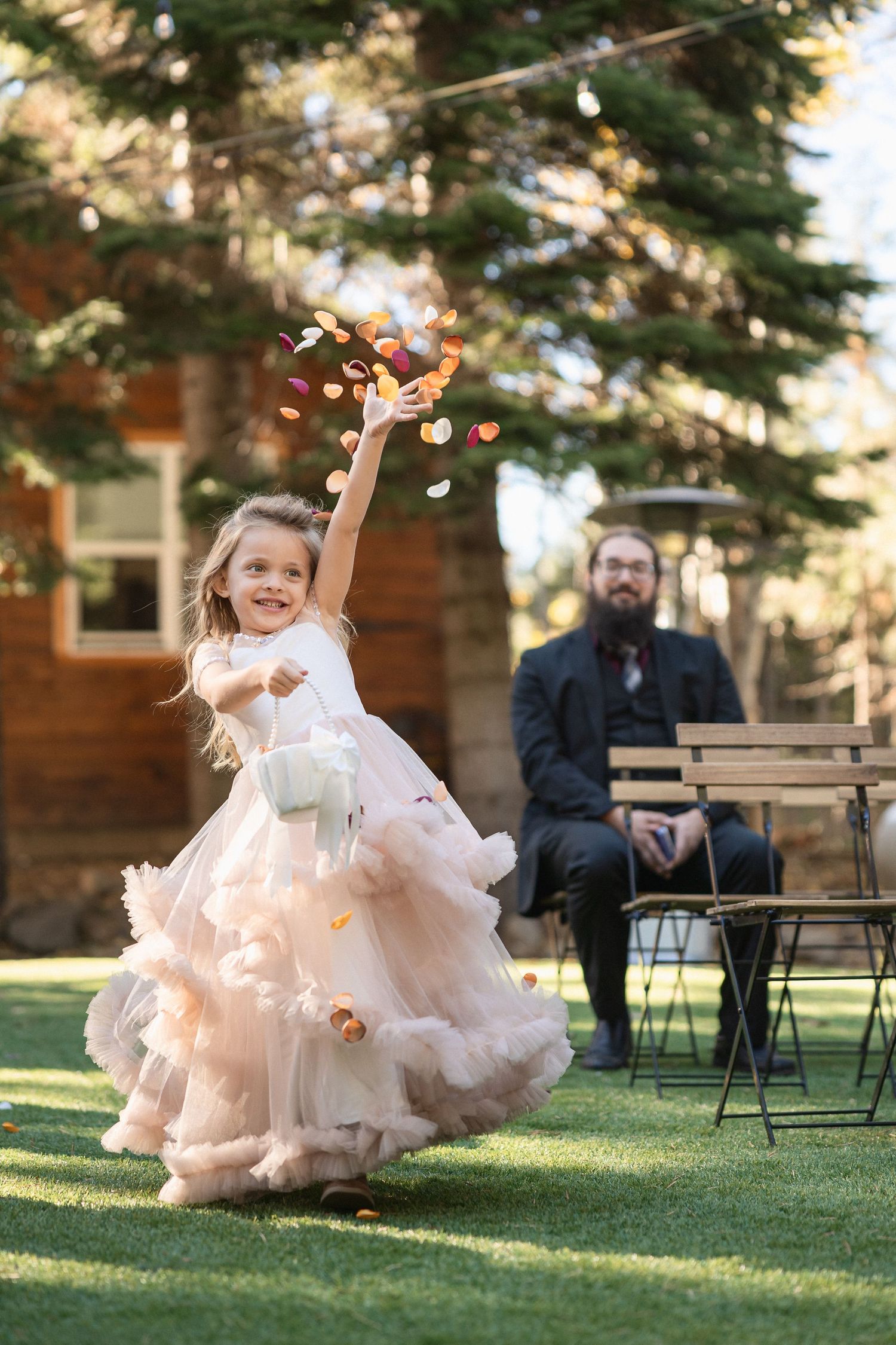 Joyful flower girl tossing petals during outdoor wedding ceremony.