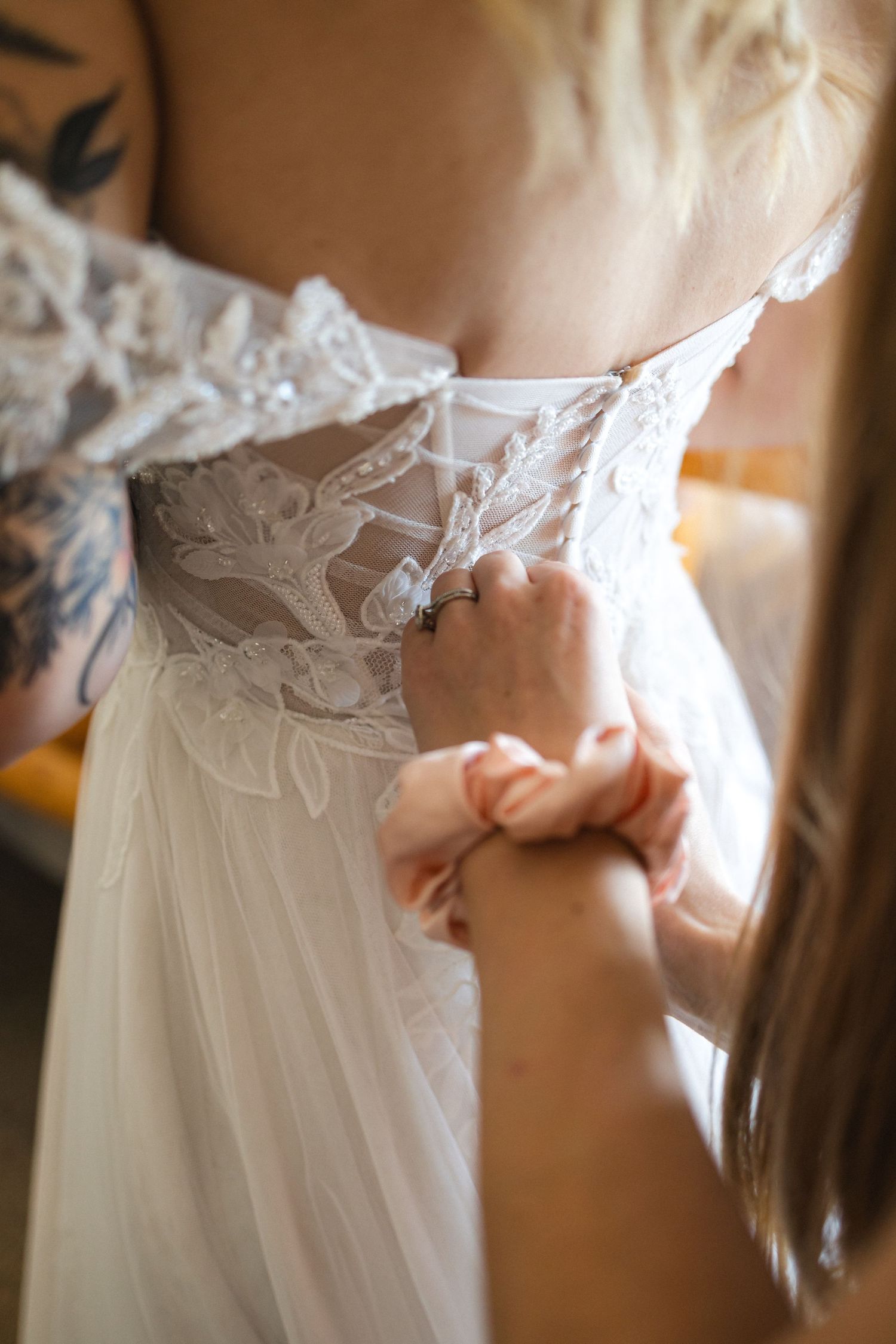 Intricate lace detailing on the back of a white wedding dress being fastened.