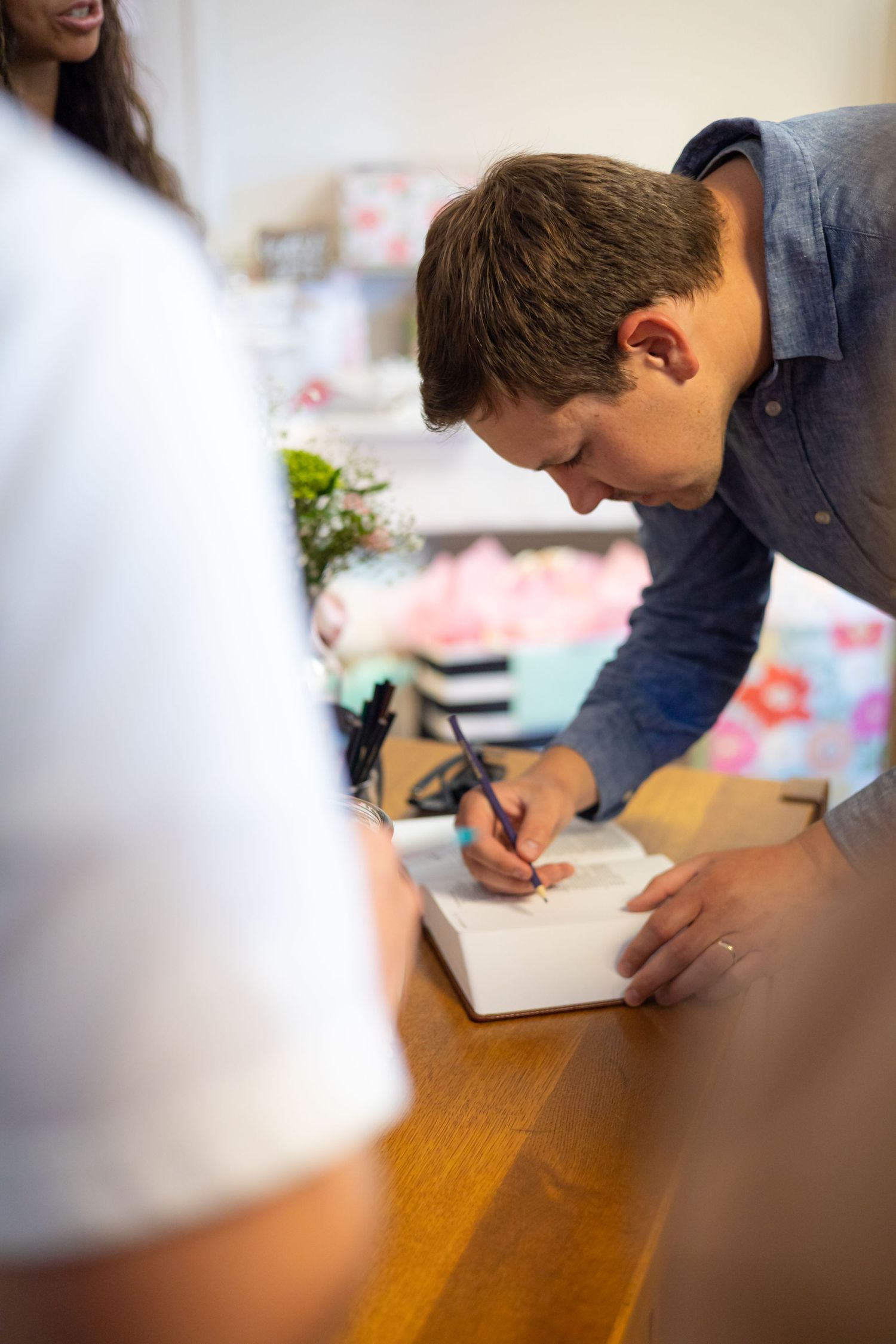 Someone signing a document on a wooden table with decorative elements in the background.