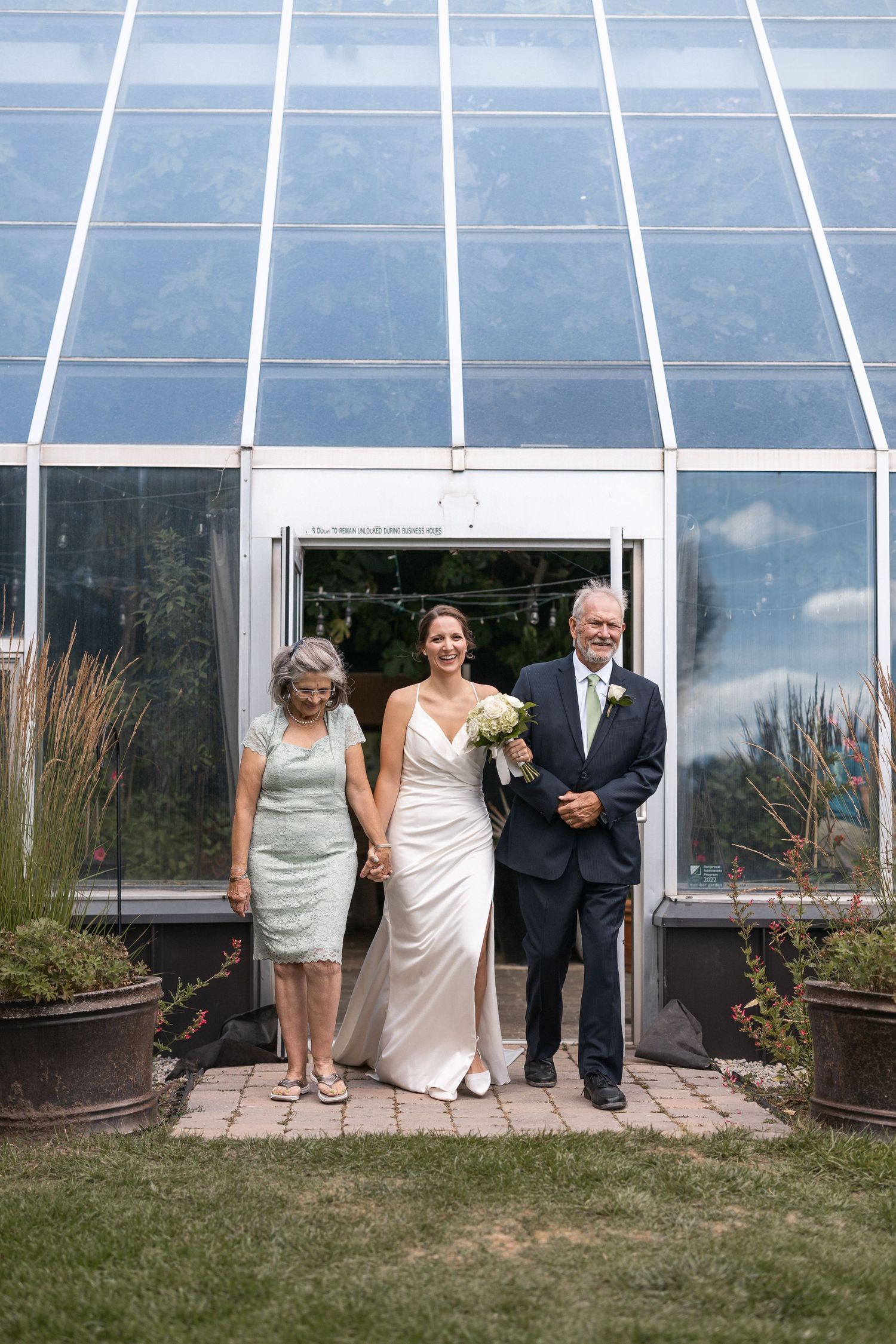 Wedding celebration outside a modern greenhouse with glass panels and landscaped garden.