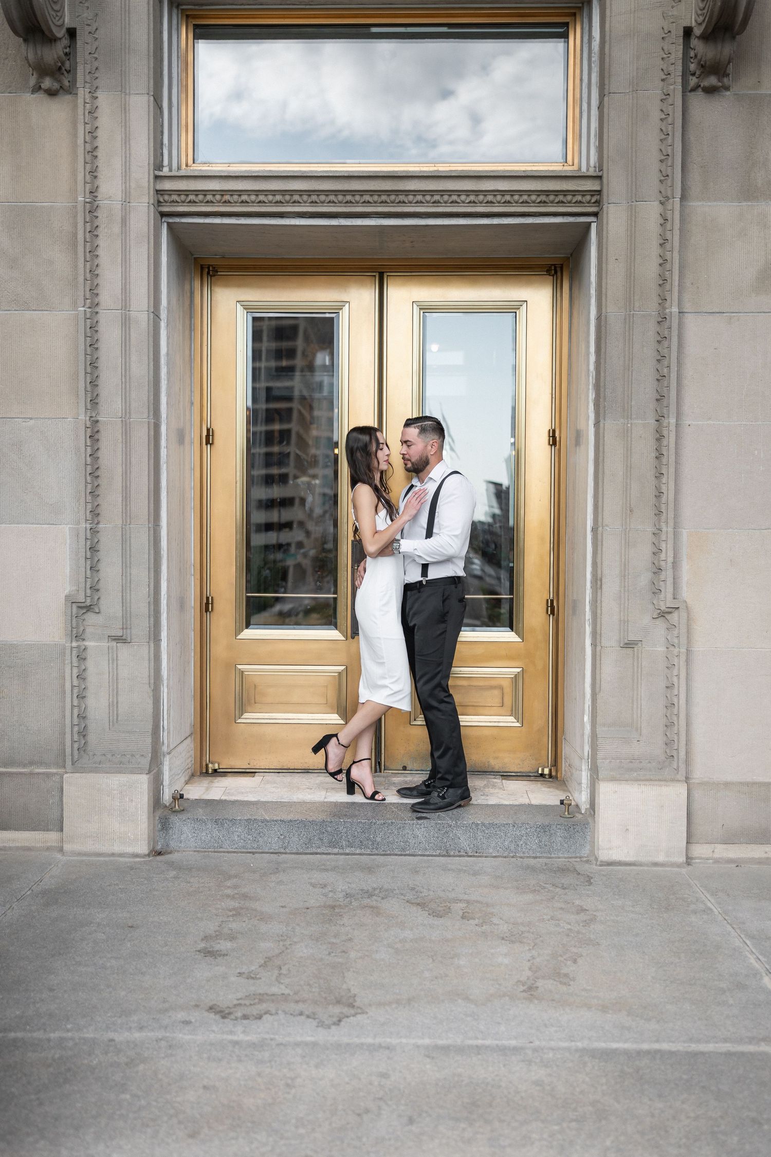 Romantic couple shares tender moments against architectural backdrop with golden doors.