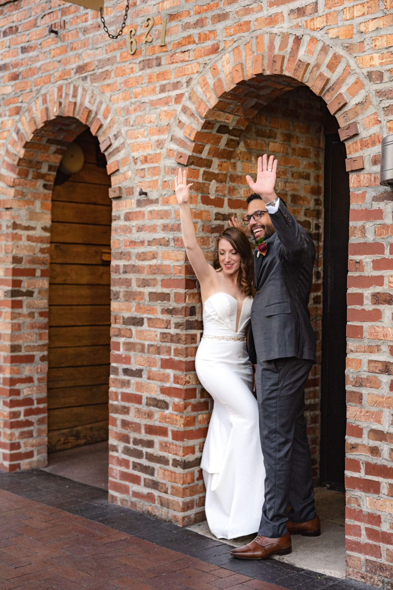 A couple celebrates with raised arms in a historic brick archway.