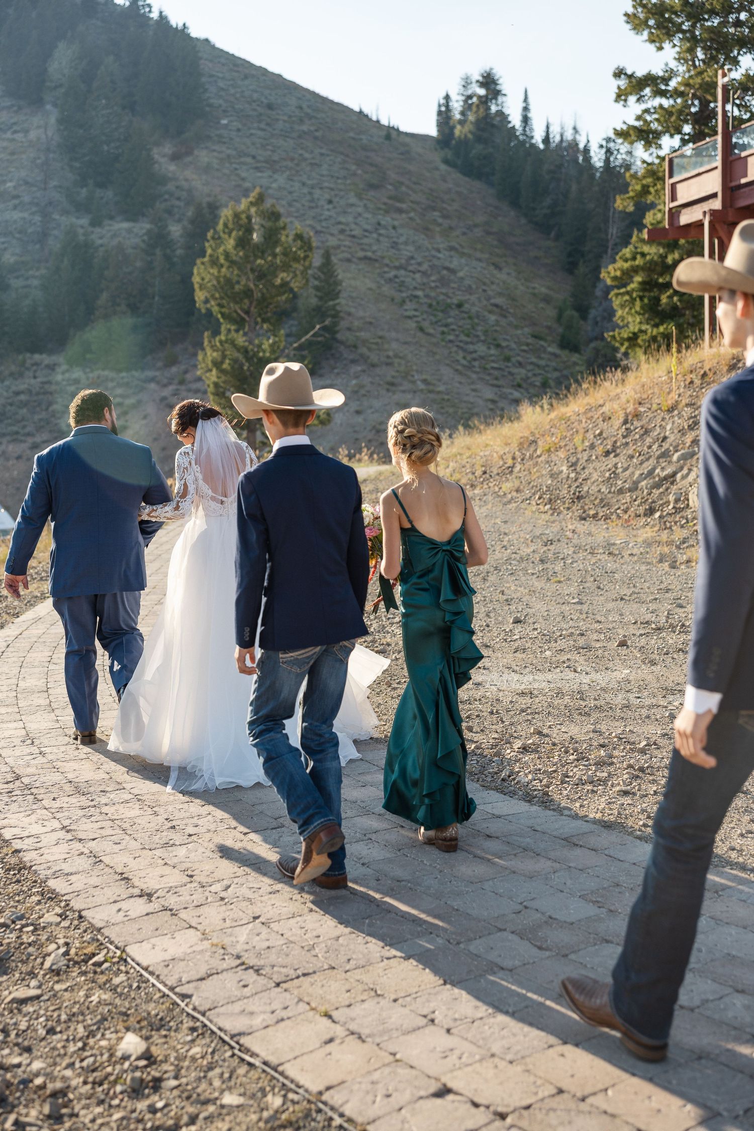 Wedding party walking along a stone path with mountains and trees in view.