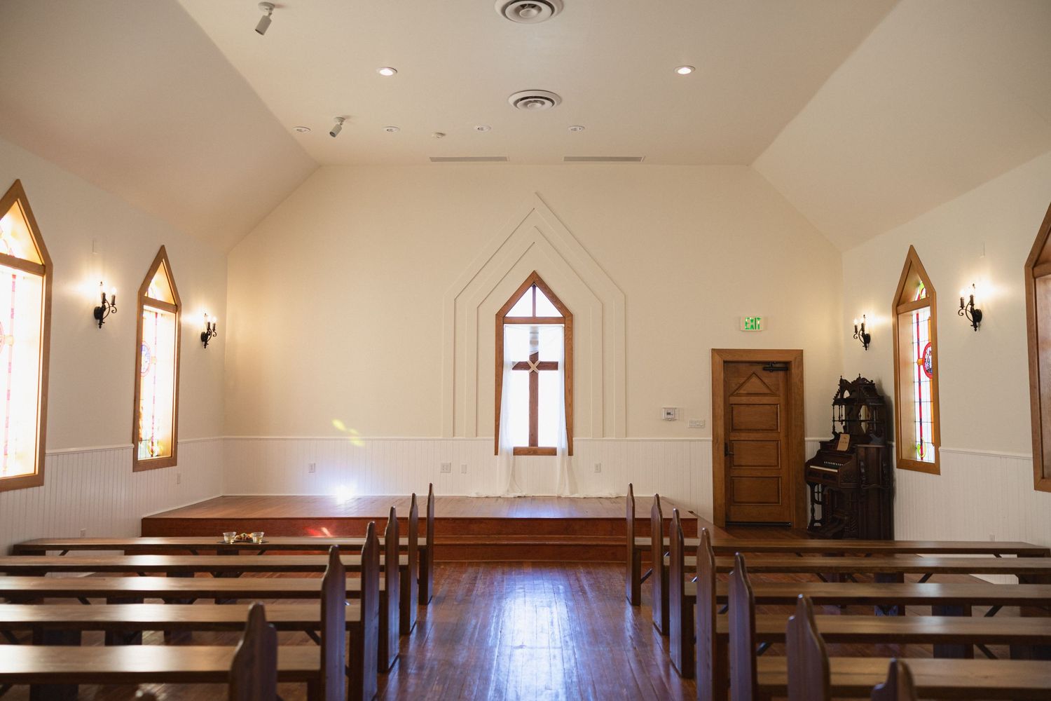 Interior of a small chapel with wooden pews and arched windows bathed in natural light.