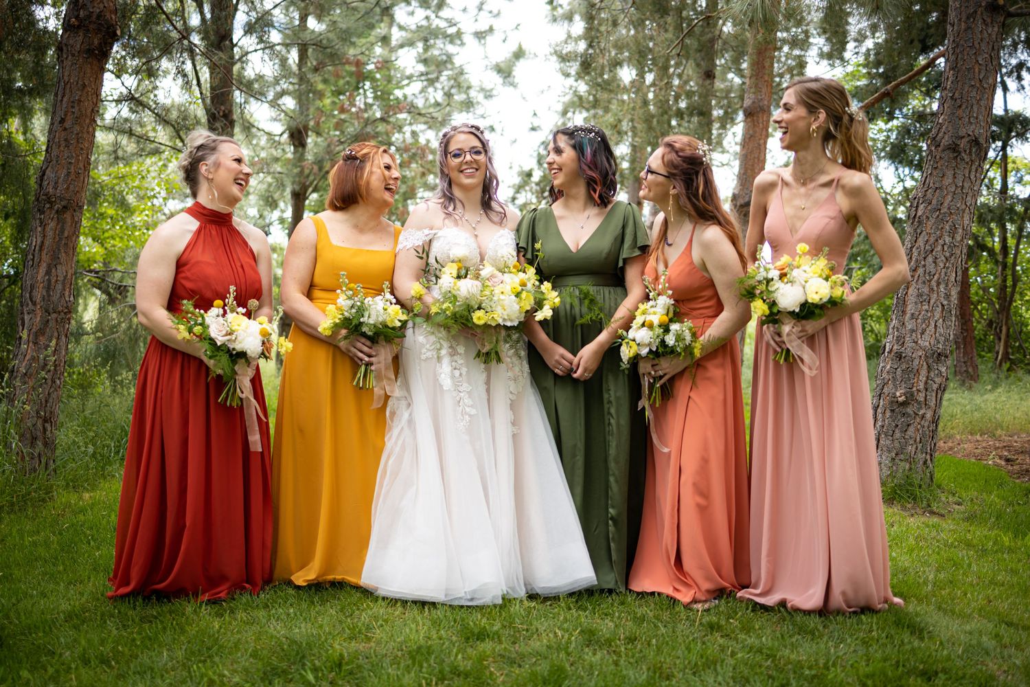 Wedding party in autumnal colors poses together in a forest setting with bridesmaids in rust and gold dresses.