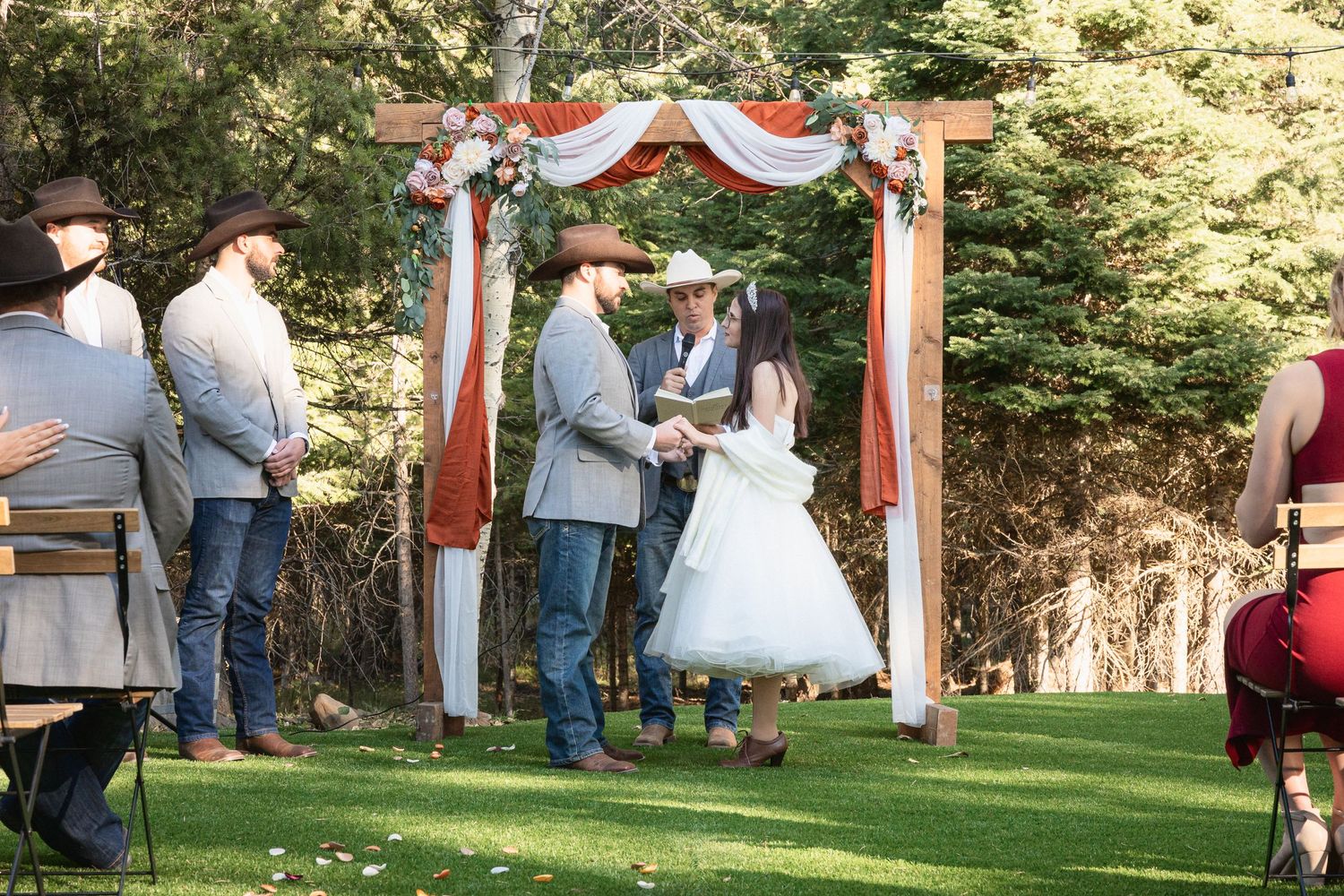 Wedding ceremony under rustic wooden arch decorated with white and coral fabric and flowers.