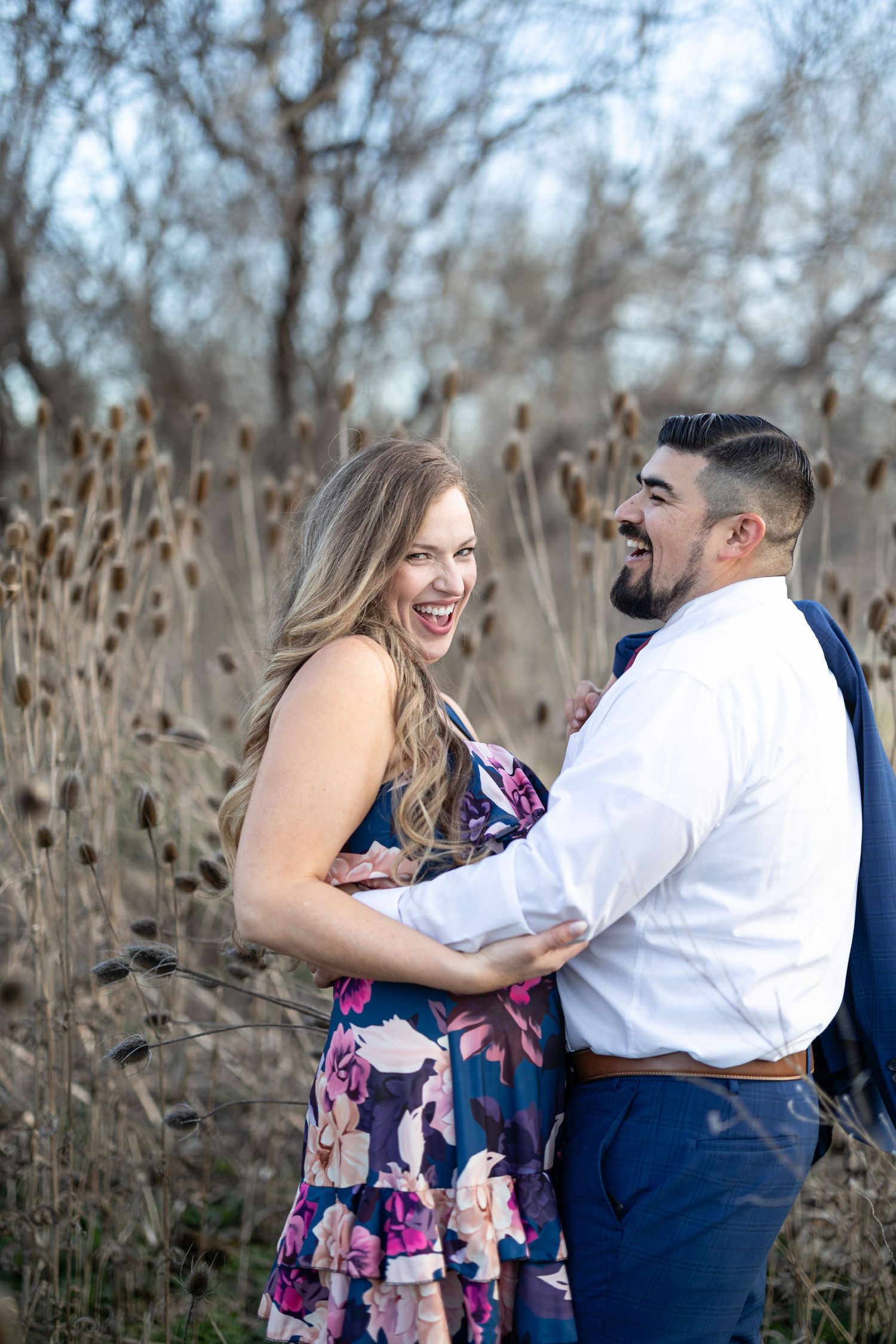 A joyful couple shares a laugh while embracing among tall dried grasses in nature.