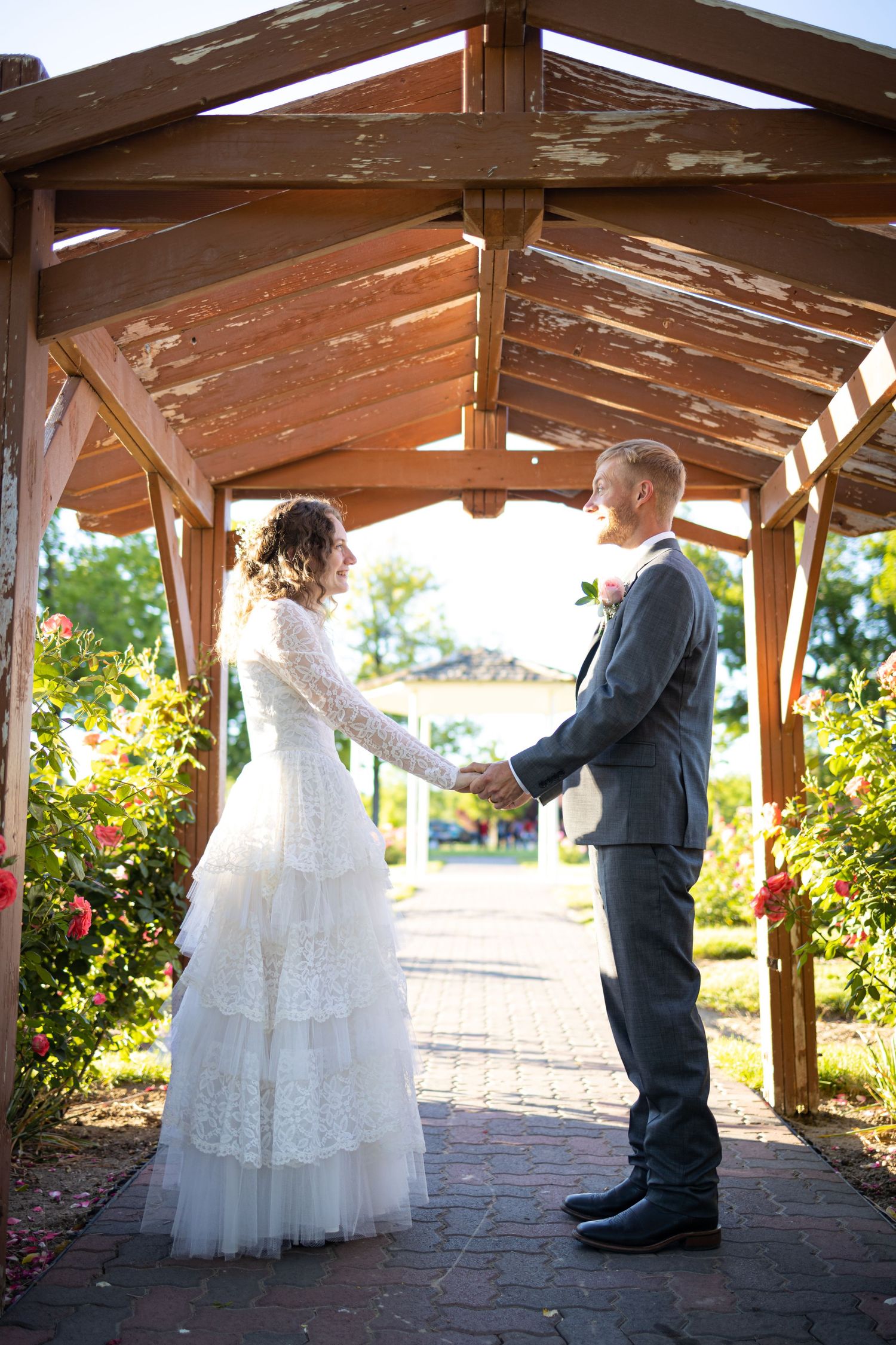 Couple sharing wedding vows under a wooden pergola in a garden setting.