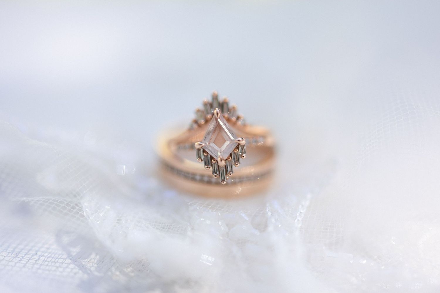 Delicate rose gold engagement ring with geometric diamond design on white lace background.