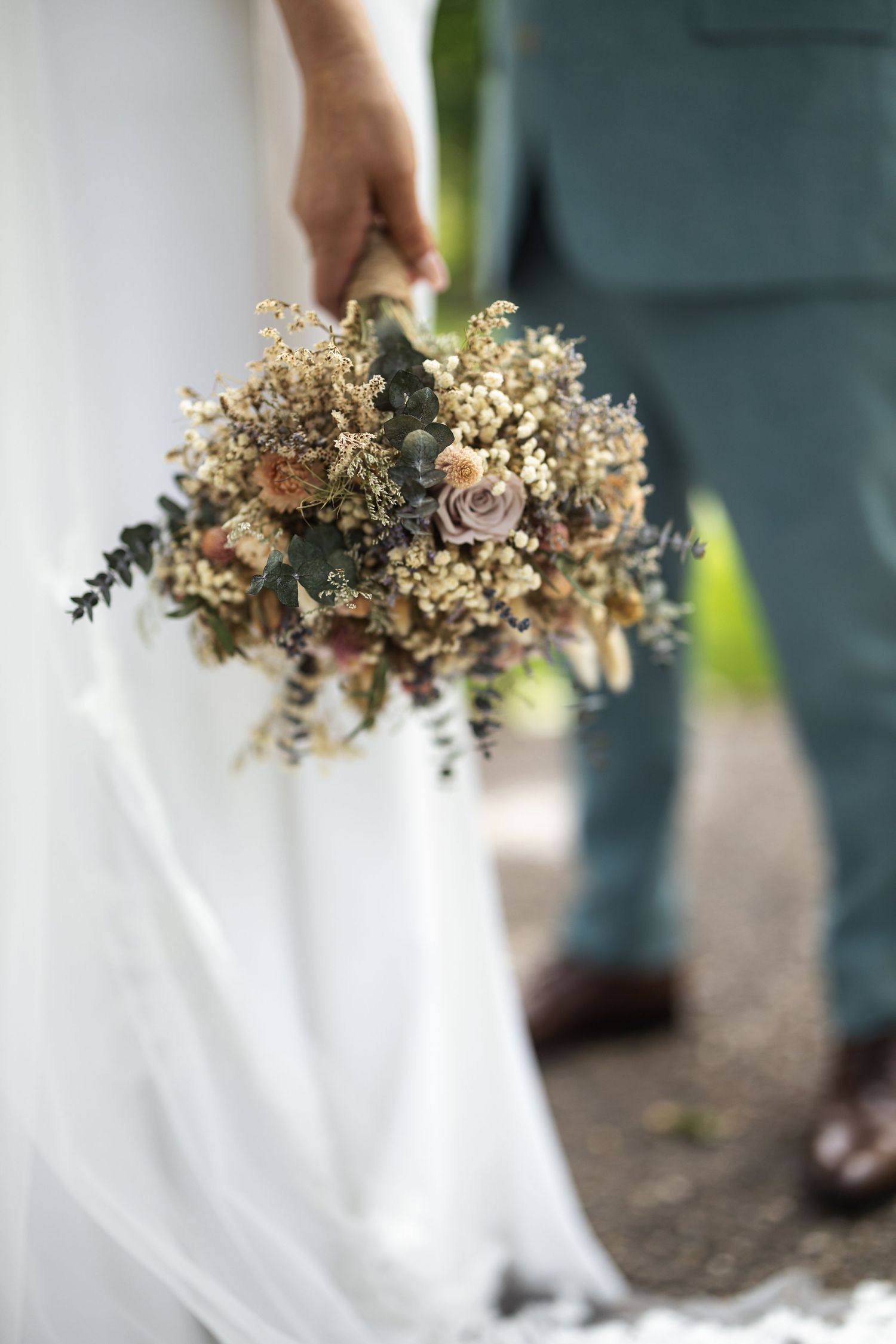 Rustic dried flower wedding bouquet with neutral tones and roses against white dress.