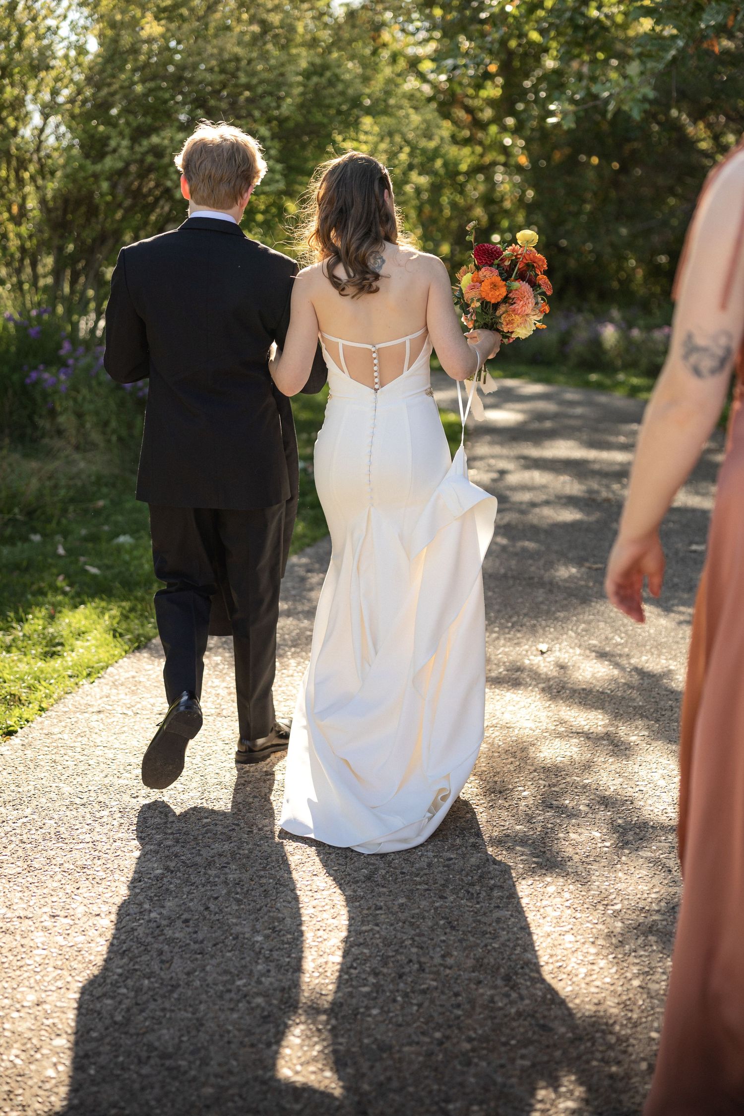 Wedding couple walking down a sunlit path with shadows cast on the ground.