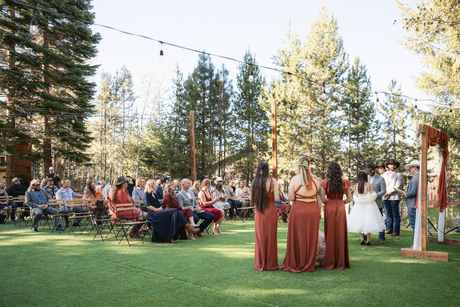 Outdoor wedding ceremony setup in a pine forest with wooden arch and guest seating.