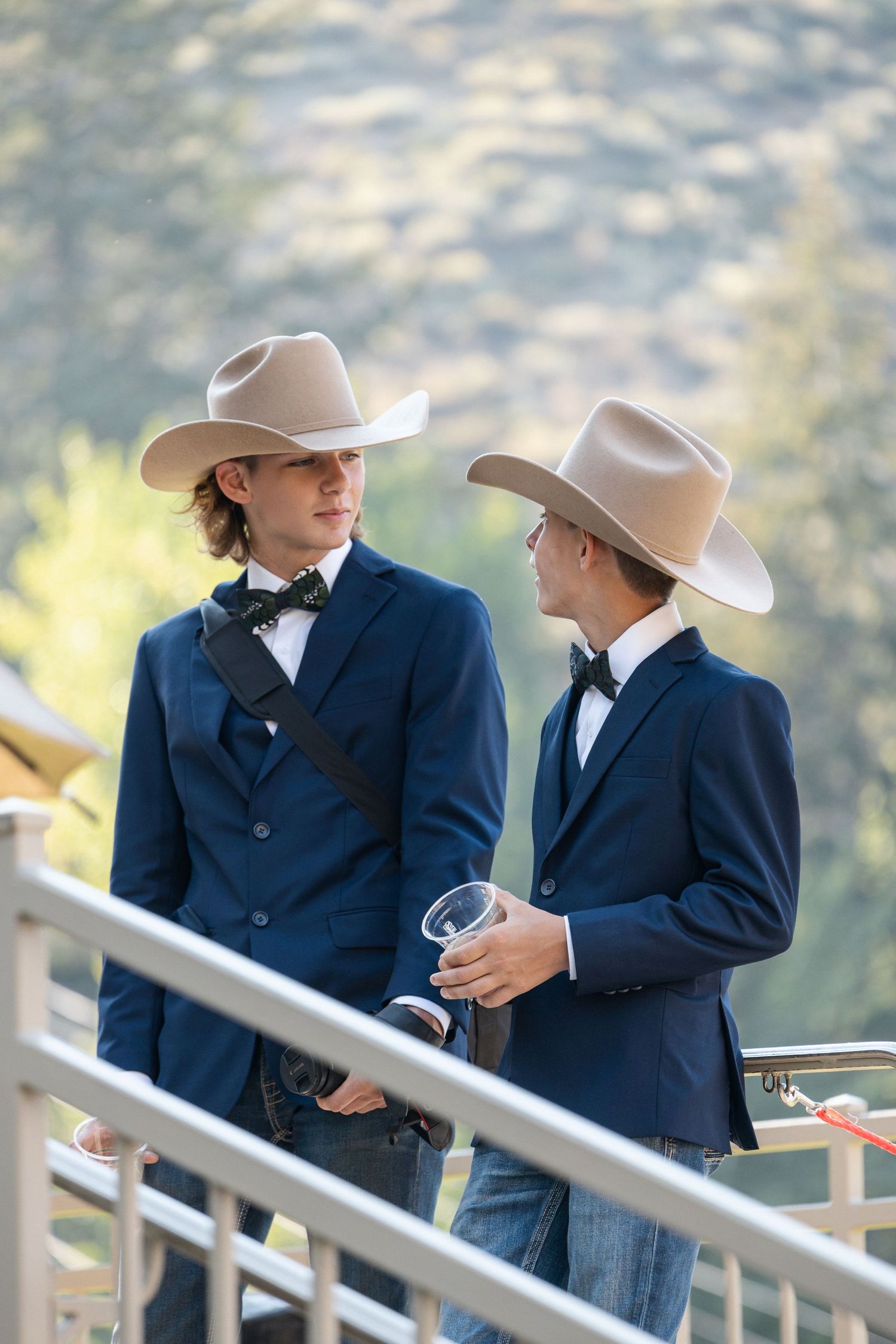 Two people in navy suits and cowboy hats conversing on an outdoor terrace.