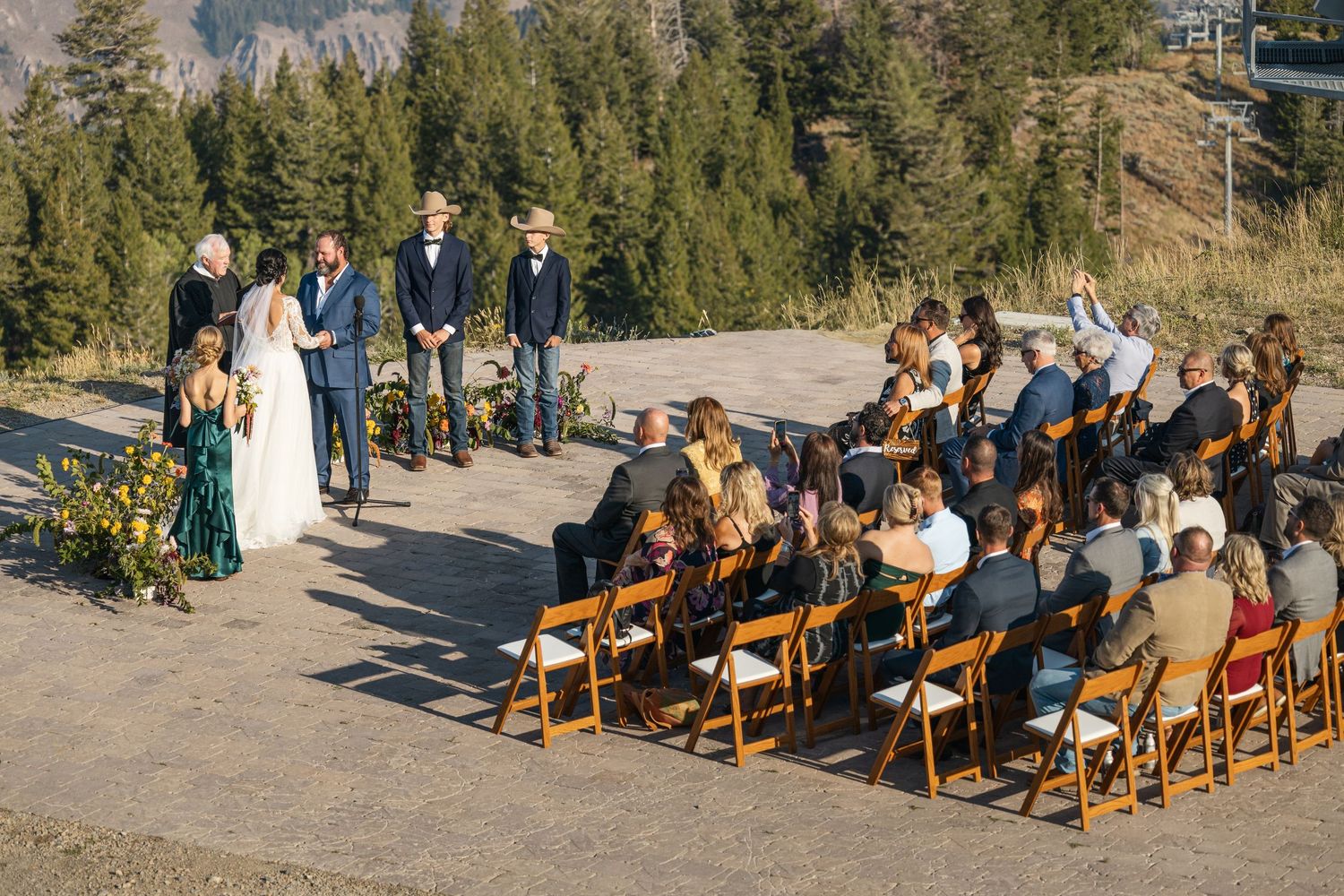 Wooden chairs arranged in rows at an outdoor mountain wedding ceremony with pine trees in the background.