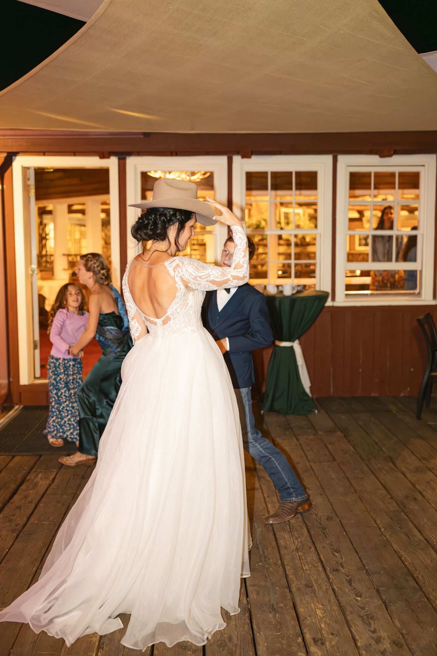 Wedding celebration on rustic wooden deck with white gowns swirling during dance.
