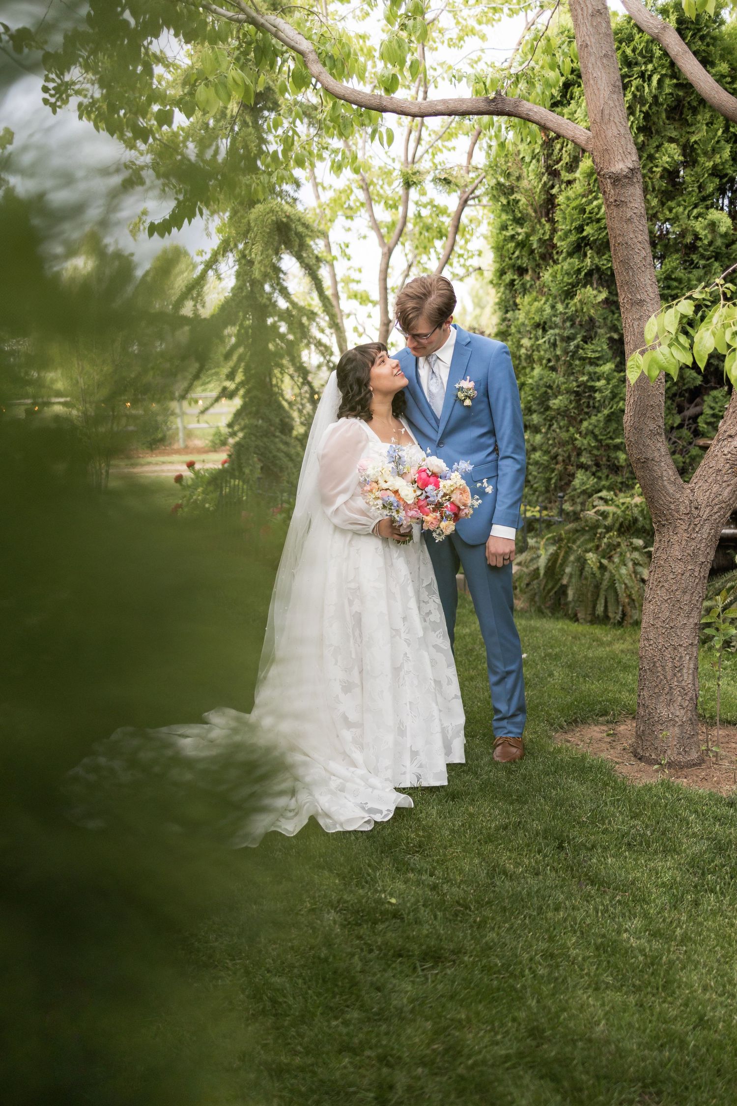 Romantic wedding portrait of couple in garden setting with lush greenery and soft lighting.