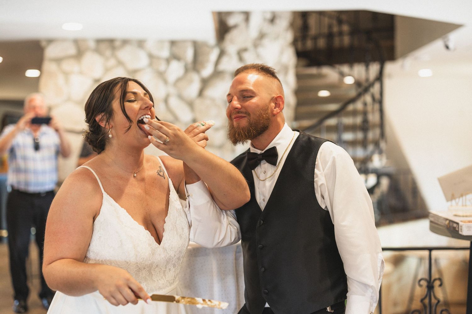 A couple playfully feeds each other wedding cake during their reception celebration.
