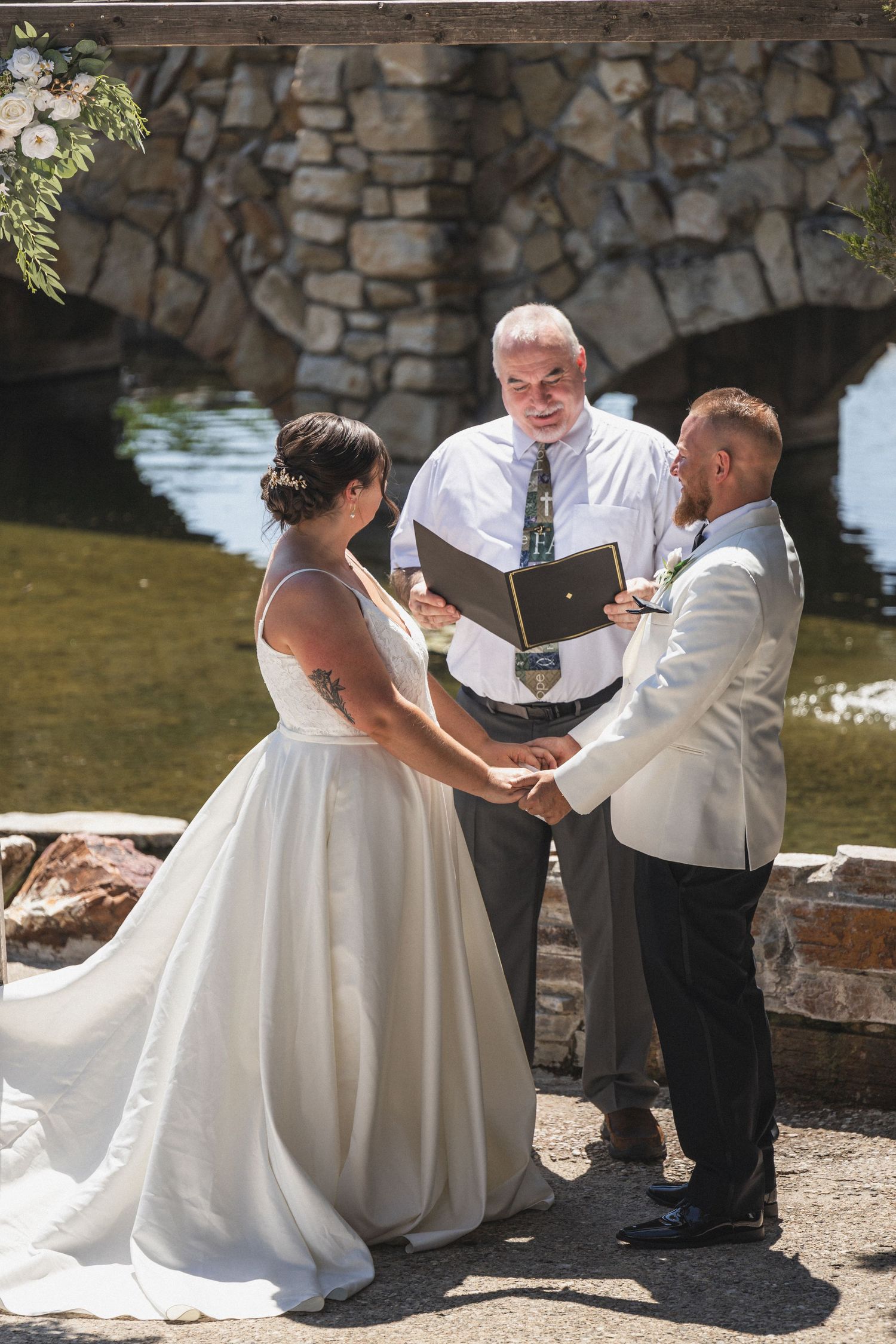 A couple exchanges wedding vows with an officiant under a stone archway during an outdoor ceremony.