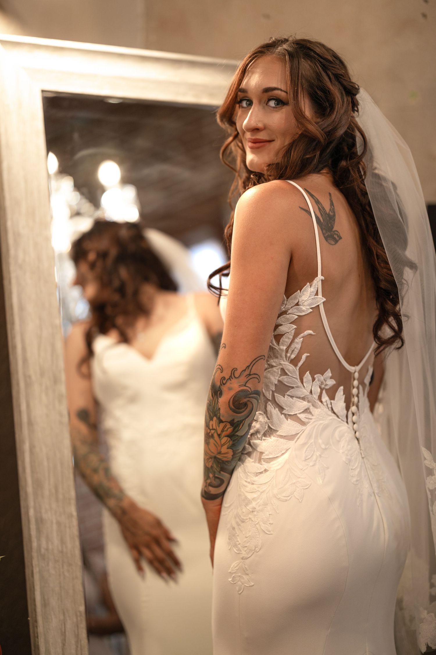 Elegant wedding dress with lace details and train photographed in mirror reflection.