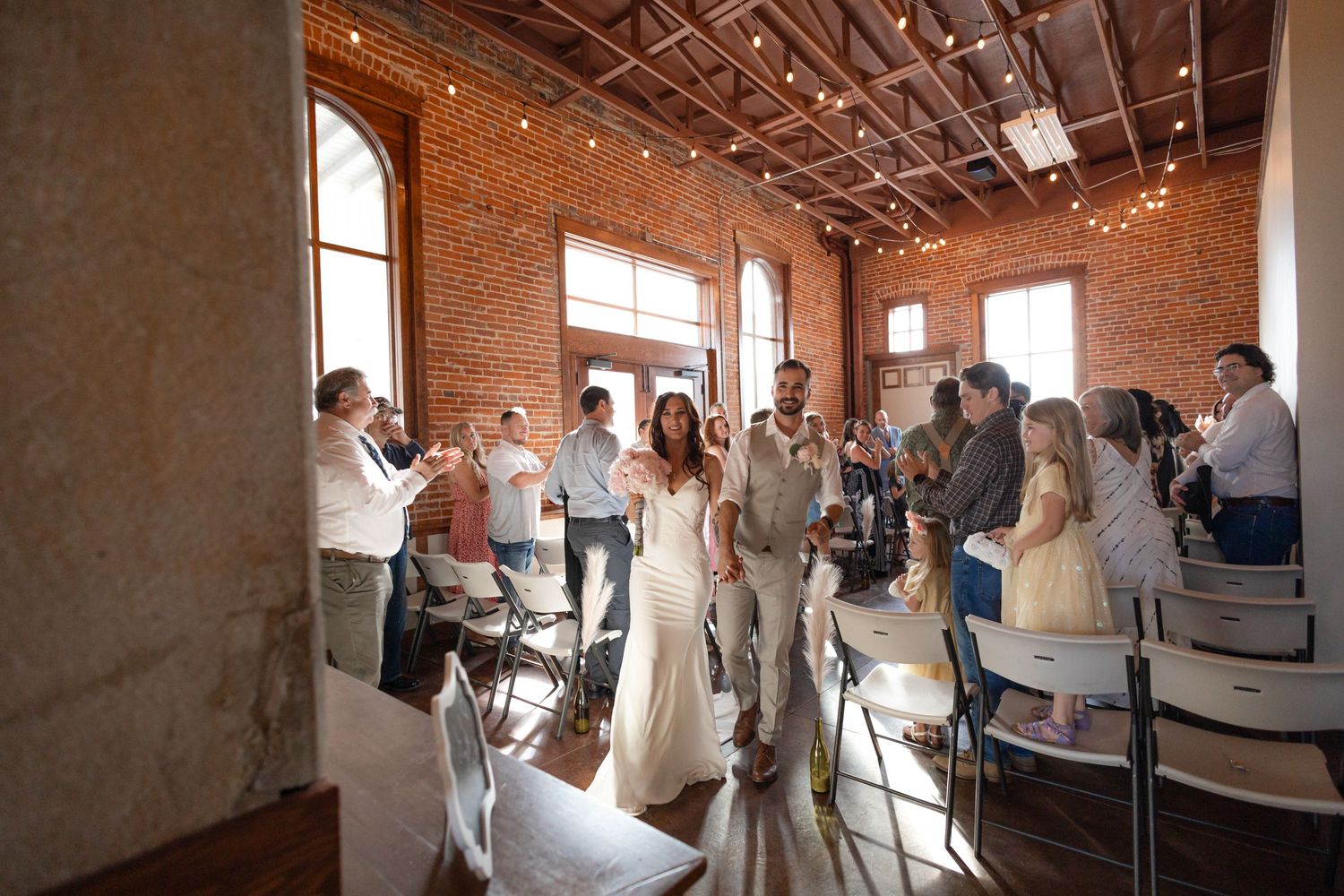 Wedding celebration in a historic brick building with string lights and arched windows.