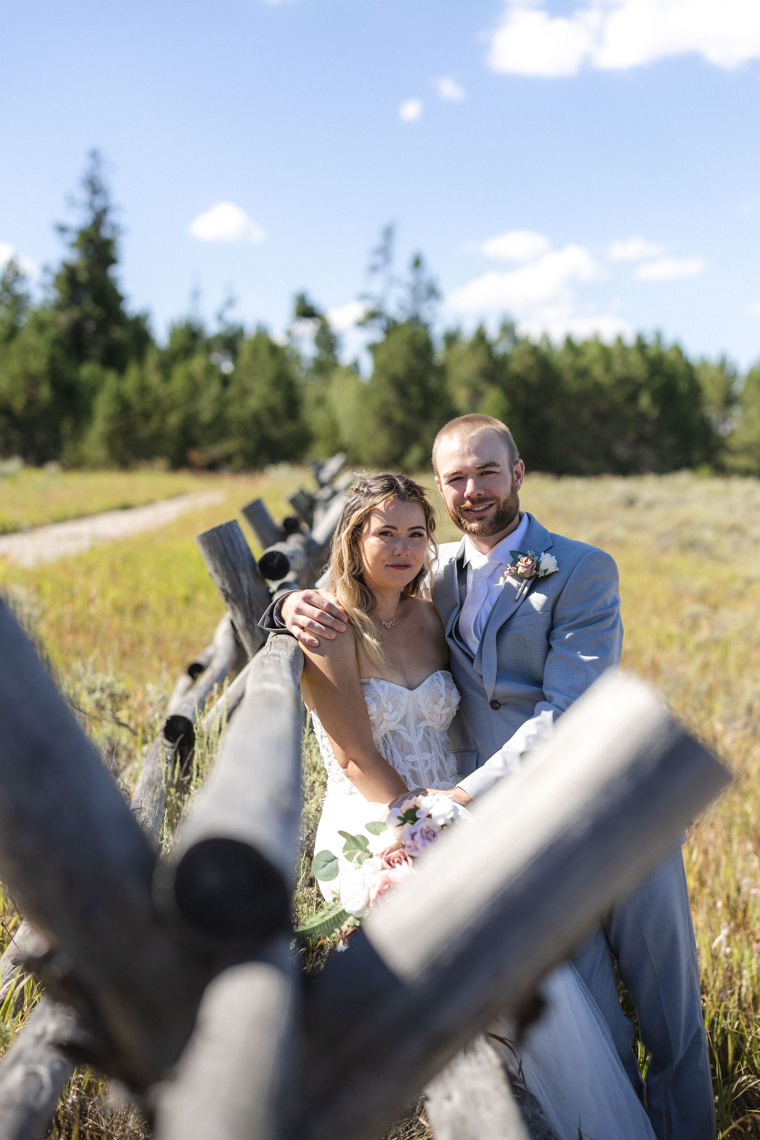 Rustic wedding photography through weathered wooden fence posts in a mountain setting.