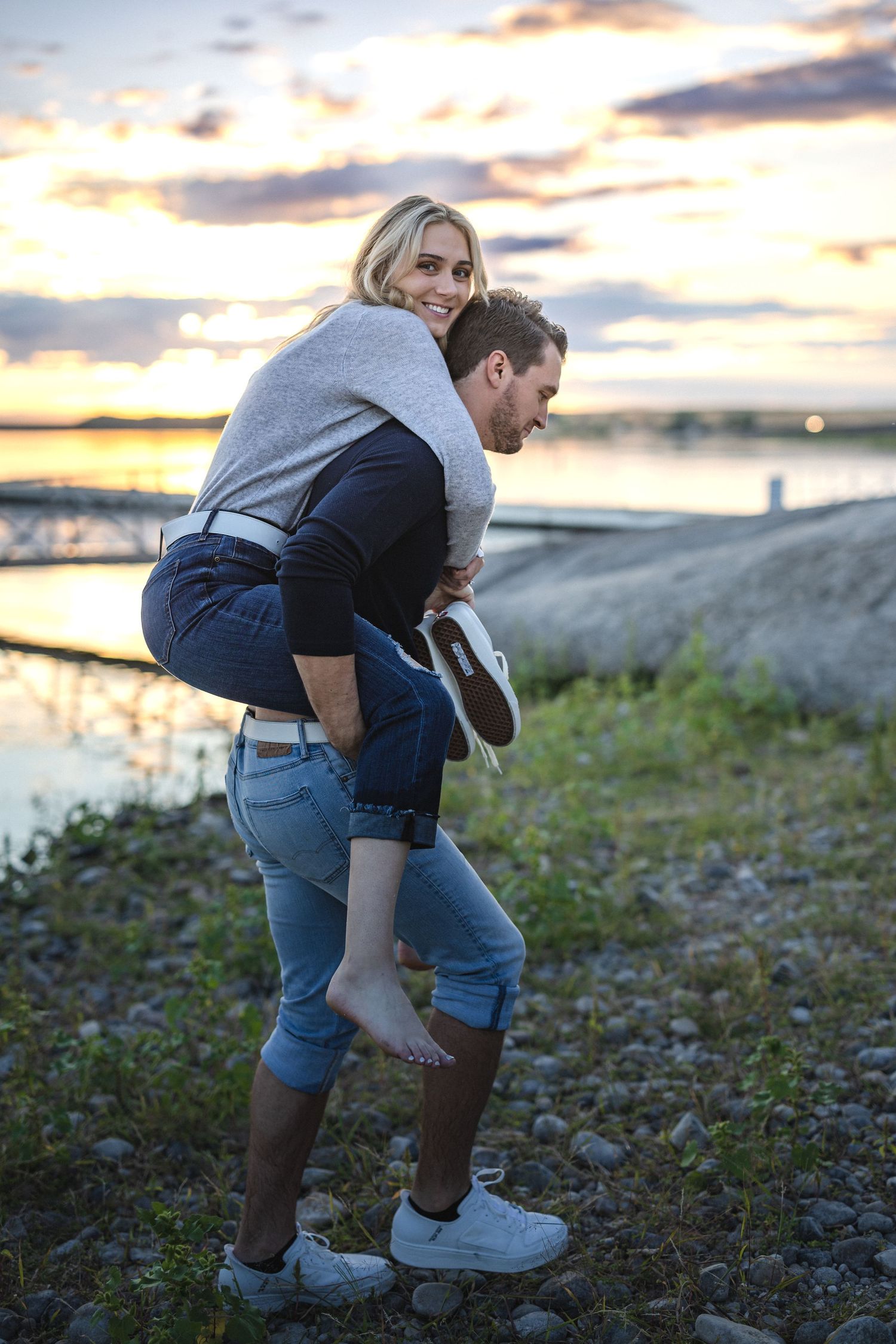 Playful outdoor moment between couple near waterfront at sunset.