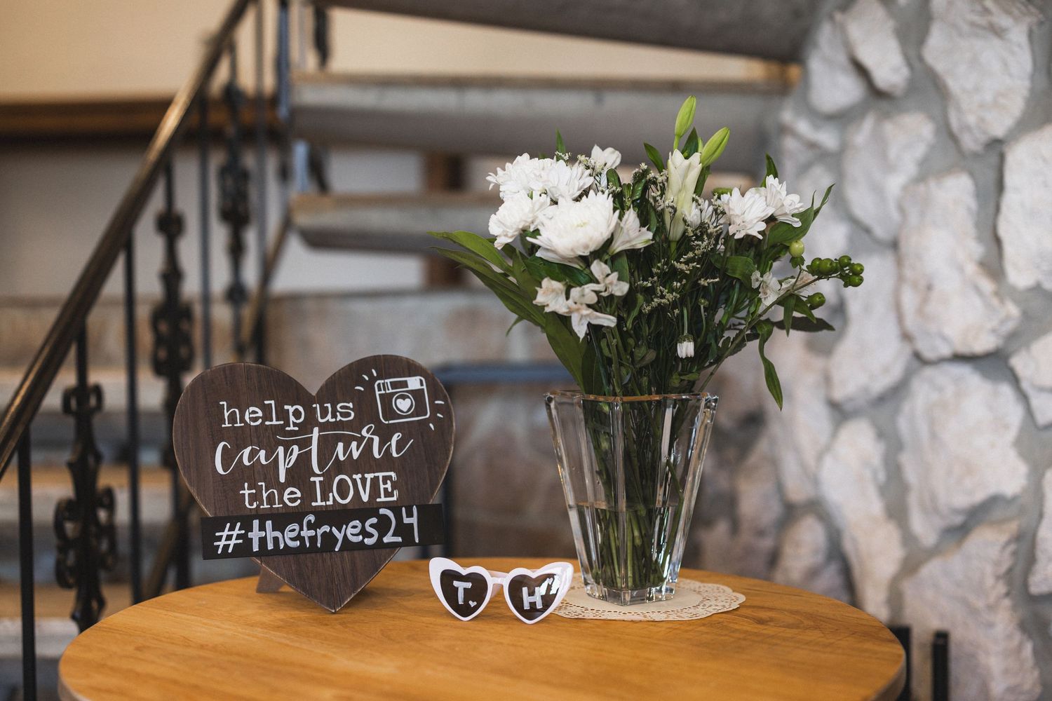 White roses in glass vase with wedding decor and sunglasses on wooden table.