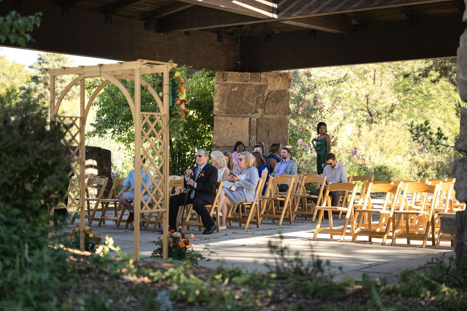 Outdoor wedding ceremony setup under a rustic wooden pavilion with rows of wooden chairs.