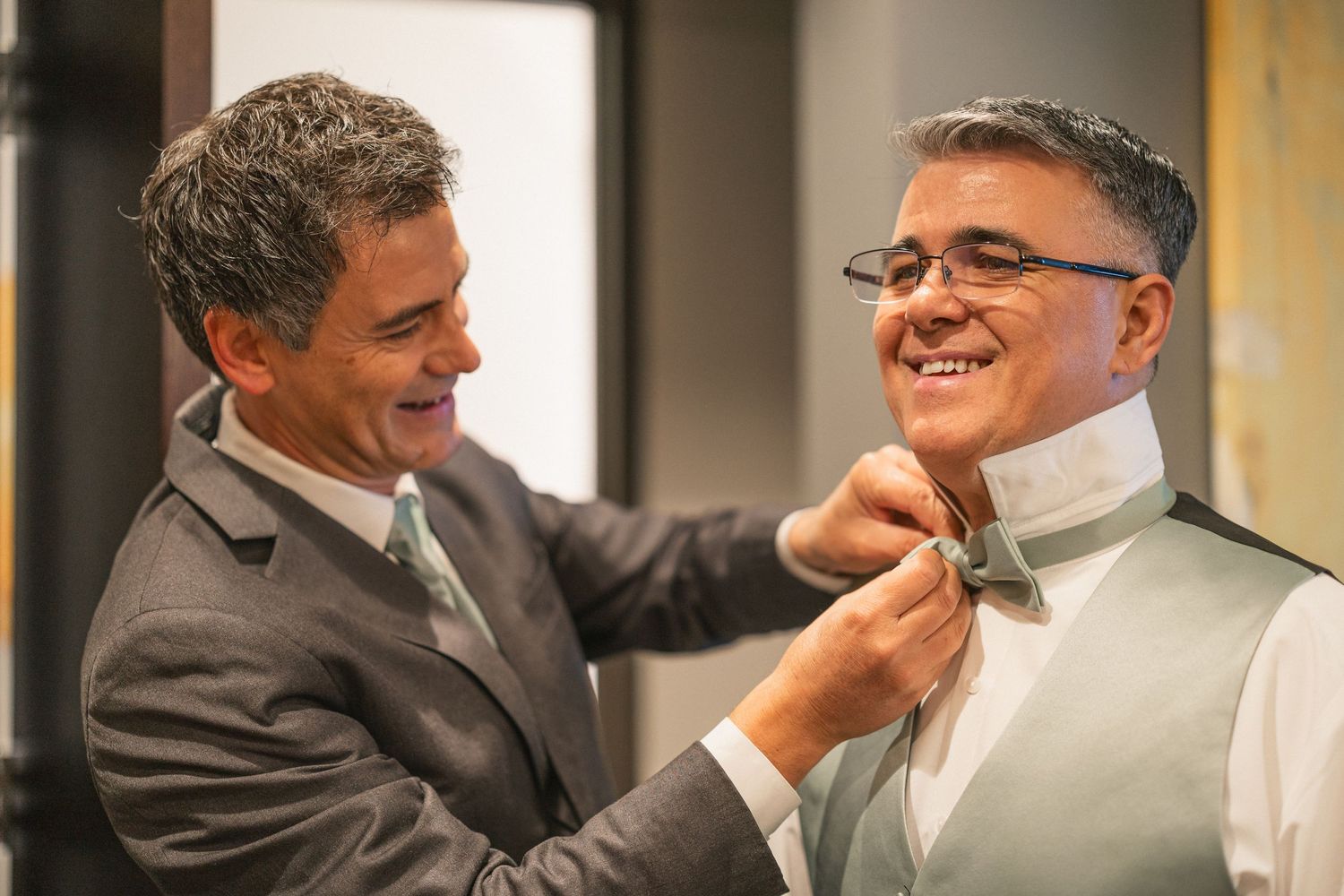 Two people share a joyful moment while adjusting formal attire.