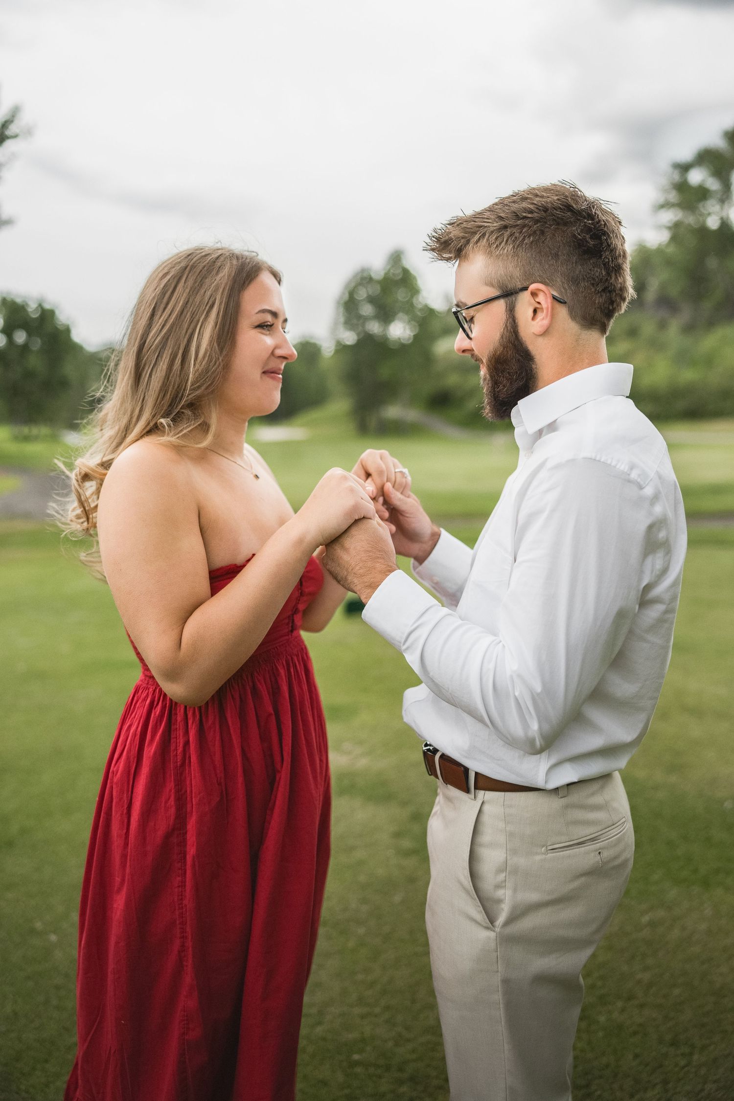 Couple in red dress and white shirt share joyful dance moves together on green lawn outdoors.
