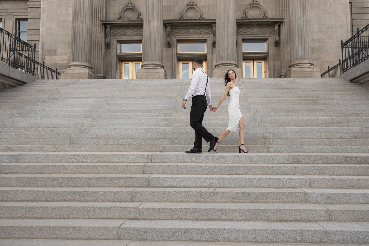 Wide view of a couple's special moment on the steps of a neoclassical building with stone columns.